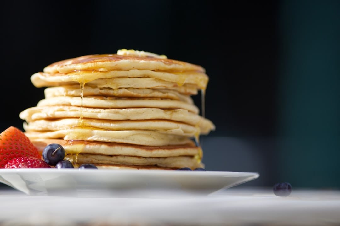 Tall stack of pancakes drizzled with syrup beside strawberries and blueberries