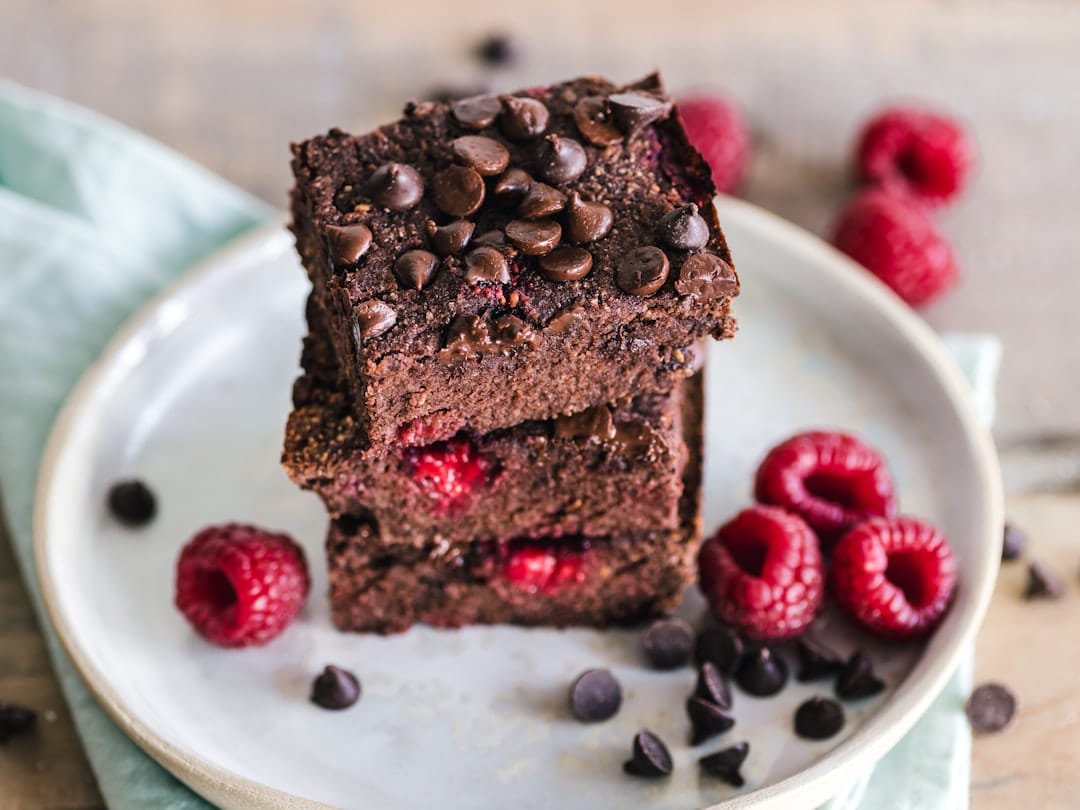 Stacked chocolate brownie squares topped with chocolate chips and raspberries