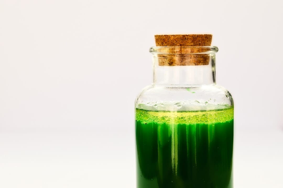Corked glass bottle filled with bright green liquid on a white background