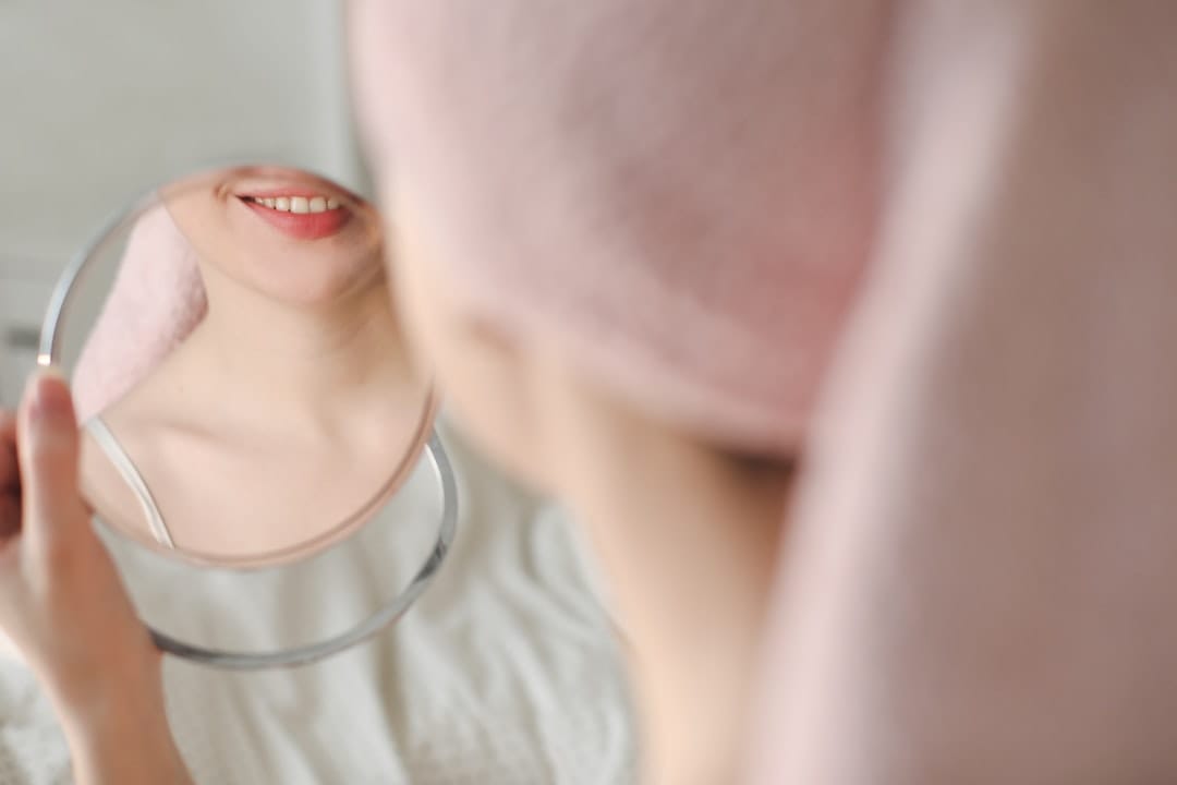 Woman smiling while checking her skin in a small round mirror