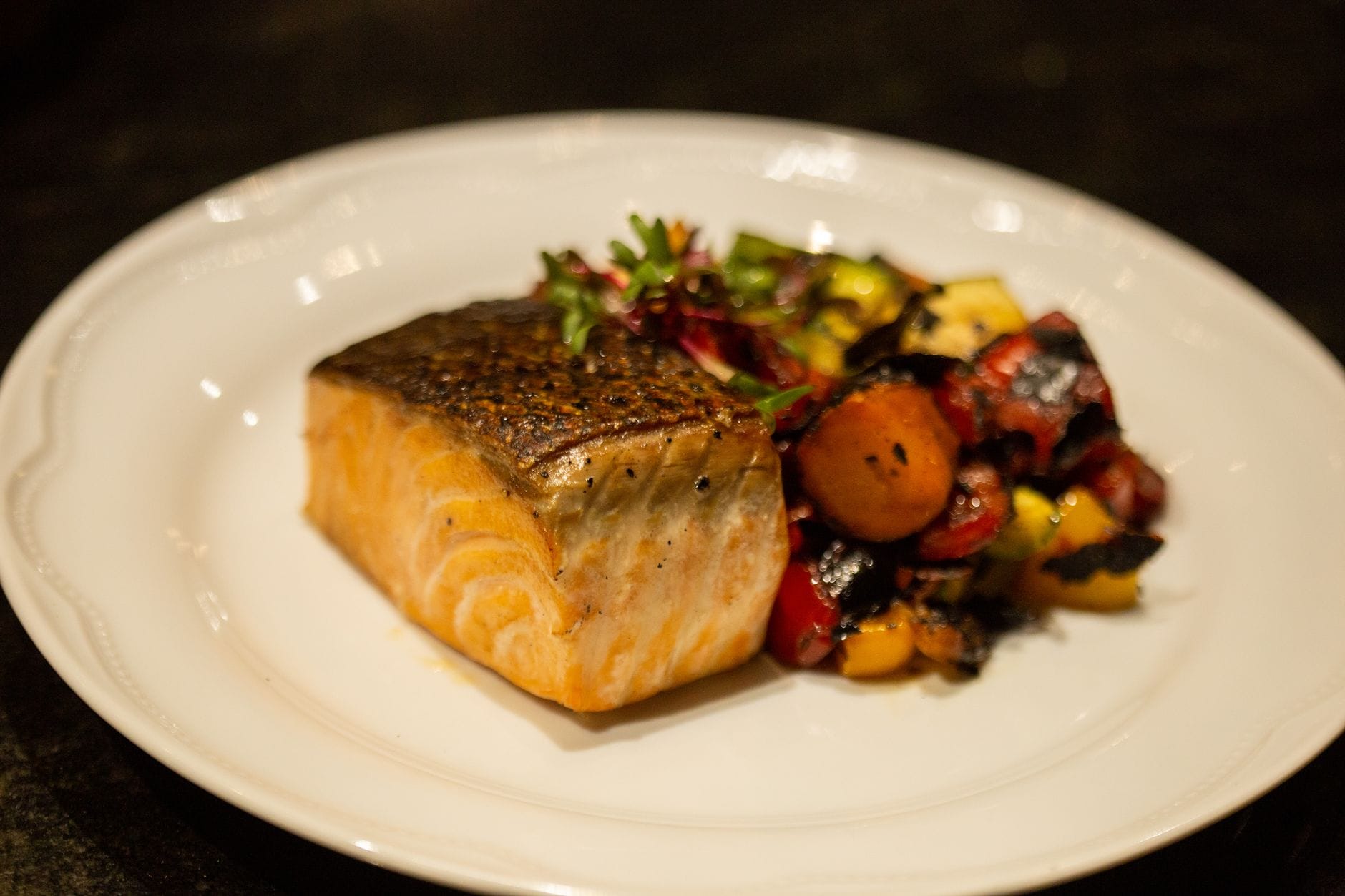Pan-seared salmon fillet with crisp skin beside roasted vegetables on white