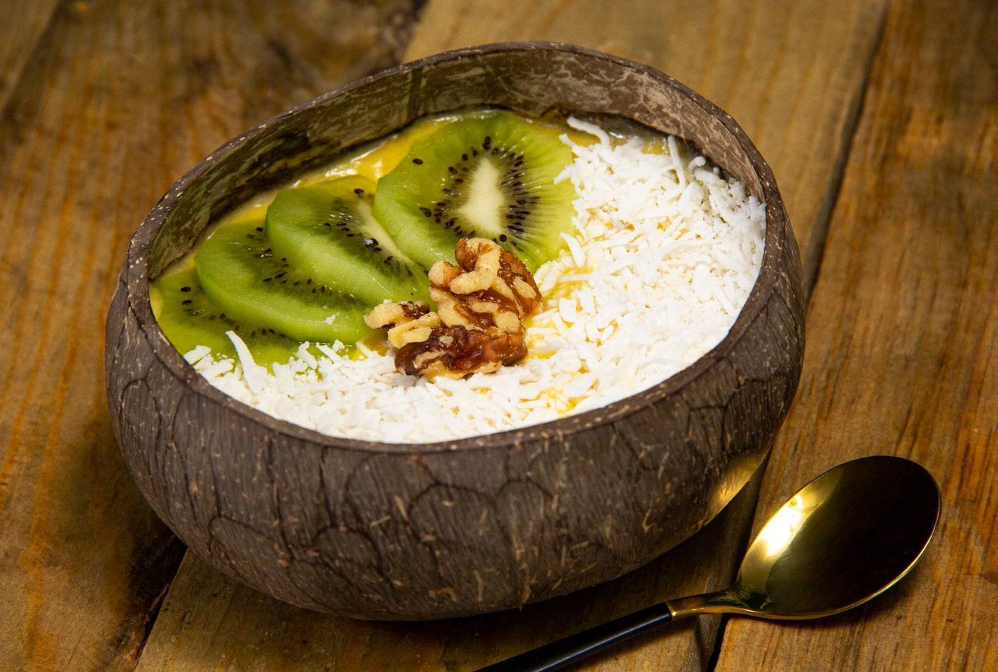 Coconut shell bowl of smoothie topped with kiwi slices, shredded coconut and walnuts