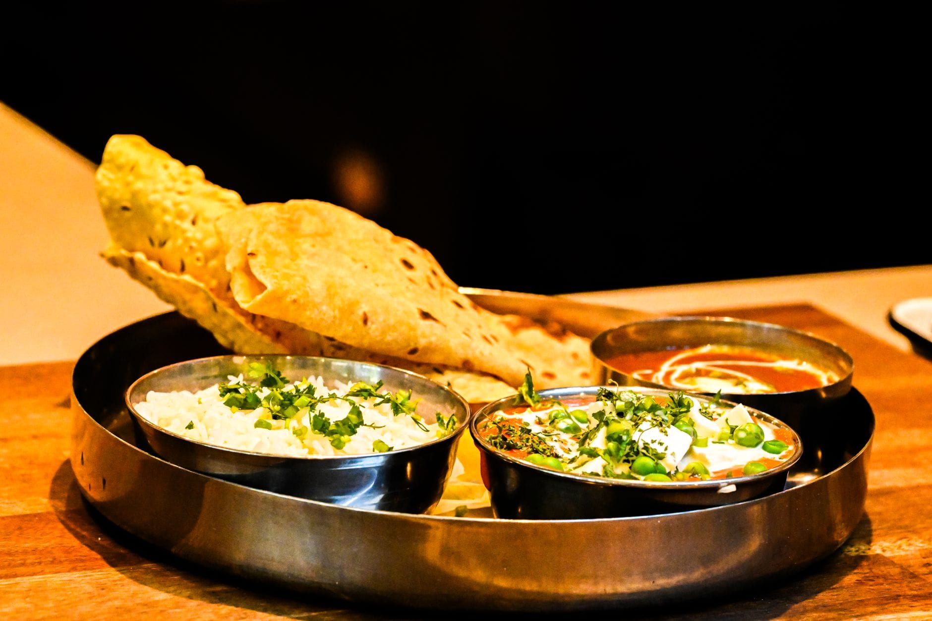 Steel thali with rice, paneer curry, tomato gravy and crisp papad