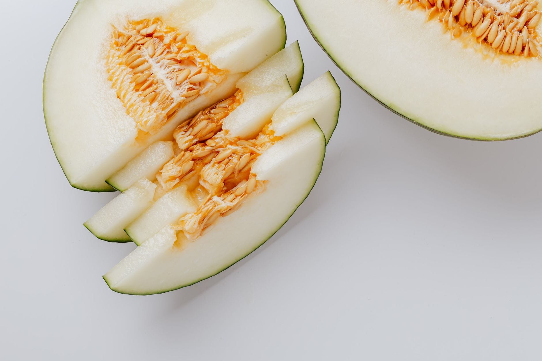 A whole honeydew melon cut open, showing pale green flesh and a centre of cream-coloured seeds