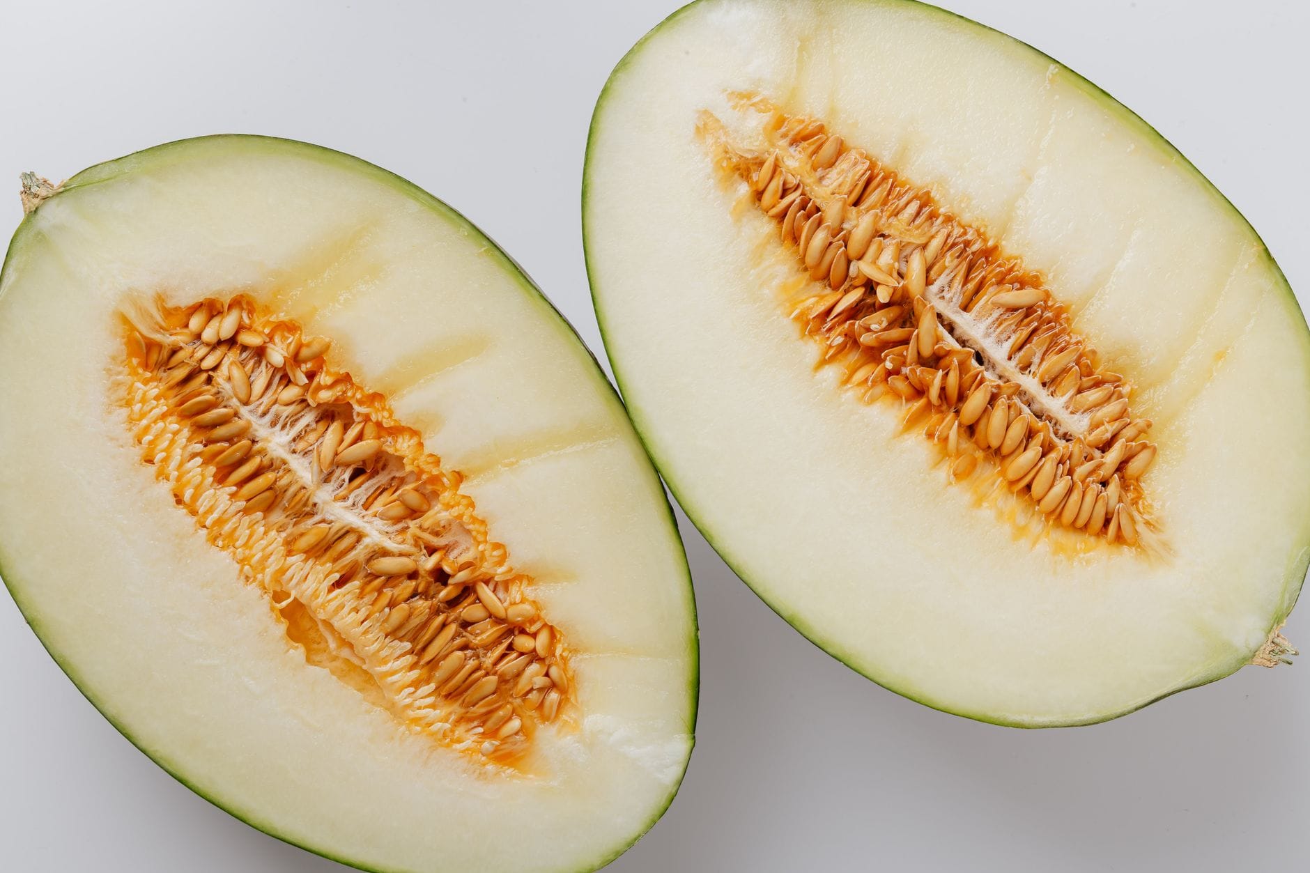 Two halves of a honeydew melon with pale green flesh and a centre of cream-coloured seeds