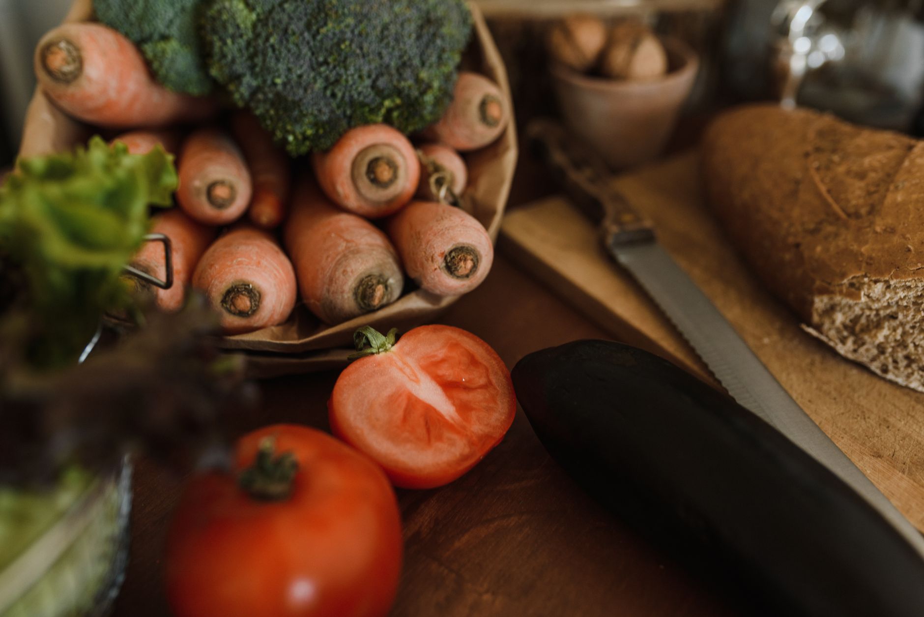 Fresh carrots, broccoli, tomatoes, and whole grain bread on a wooden table