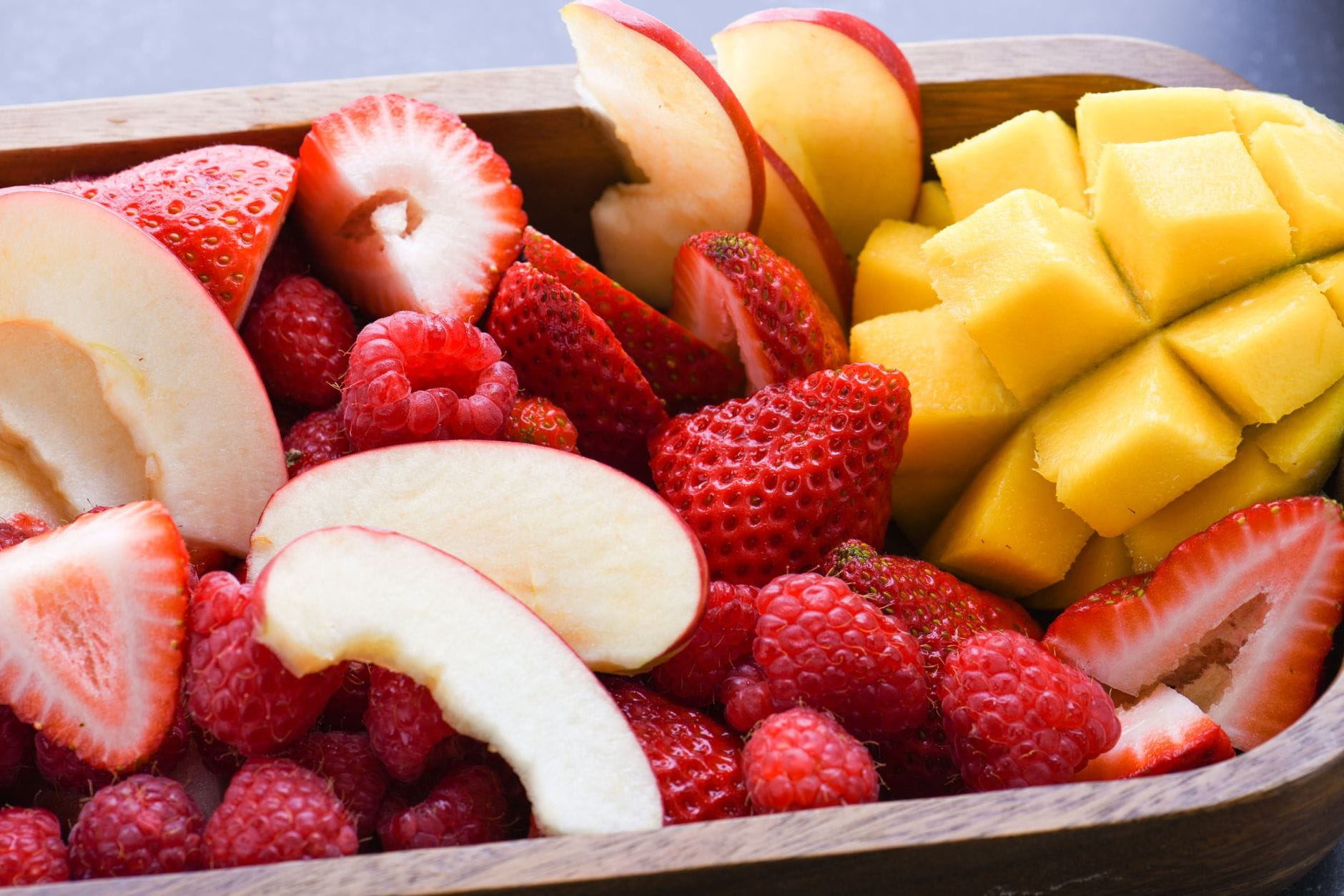 Wooden bowl piled with strawberries, raspberries, apple, and mango