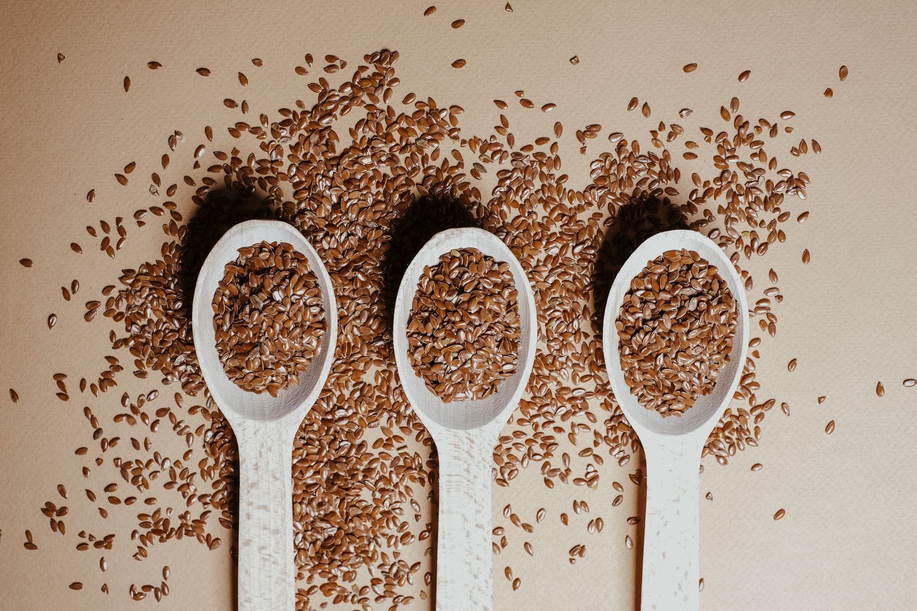 Ground and whole flaxseeds spilling from a small wooden bowl on linen