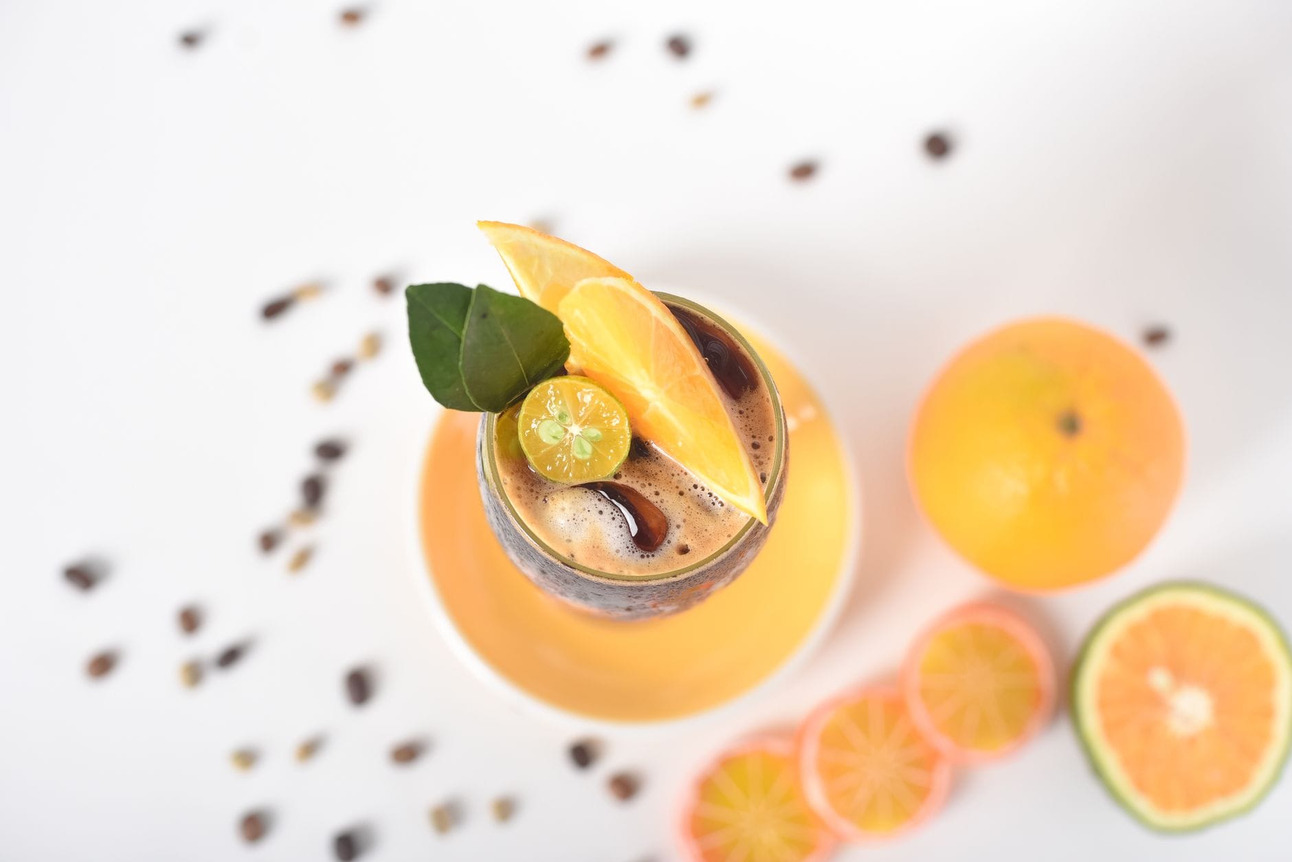 Iced black coffee in a glass garnished with orange wedge, calamansi and leaves