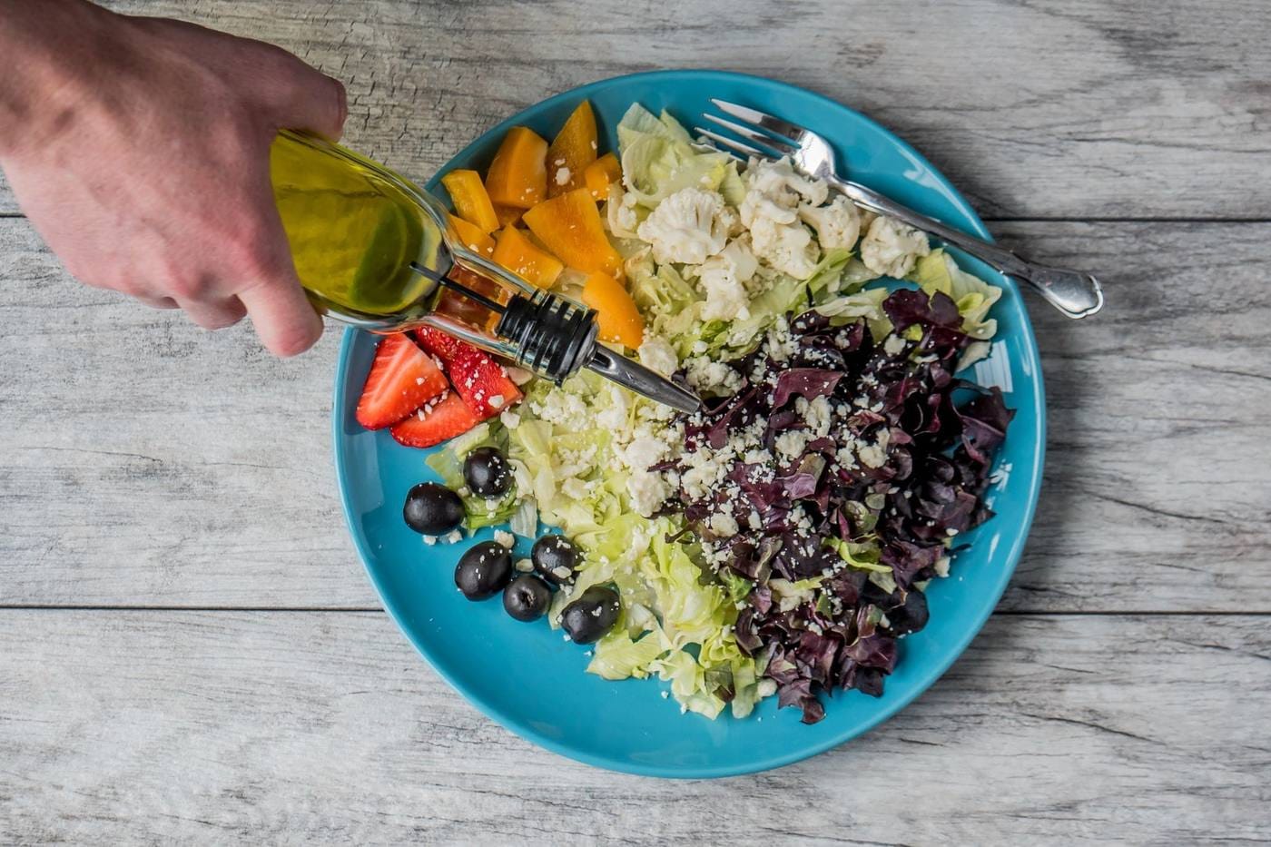 Hand pouring olive oil over a salad of feta and vegetables