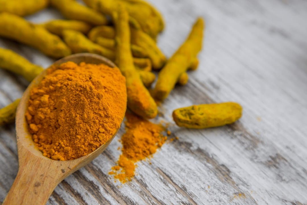 Wooden spoon heaped with orange turmeric powder beside dried turmeric roots