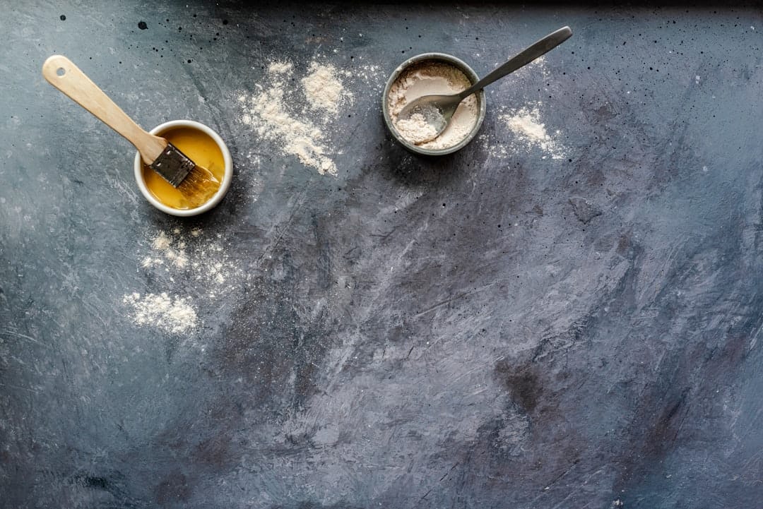 Small bowls of oil and flour set on a dark surface