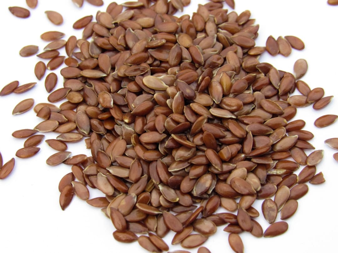 Loose pile of glossy brown flaxseeds on a white surface