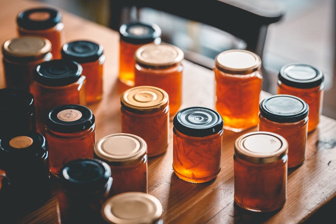 Rows of glass jars filled with orange-amber preserve and sealed with metal lids, standing on a wooden table