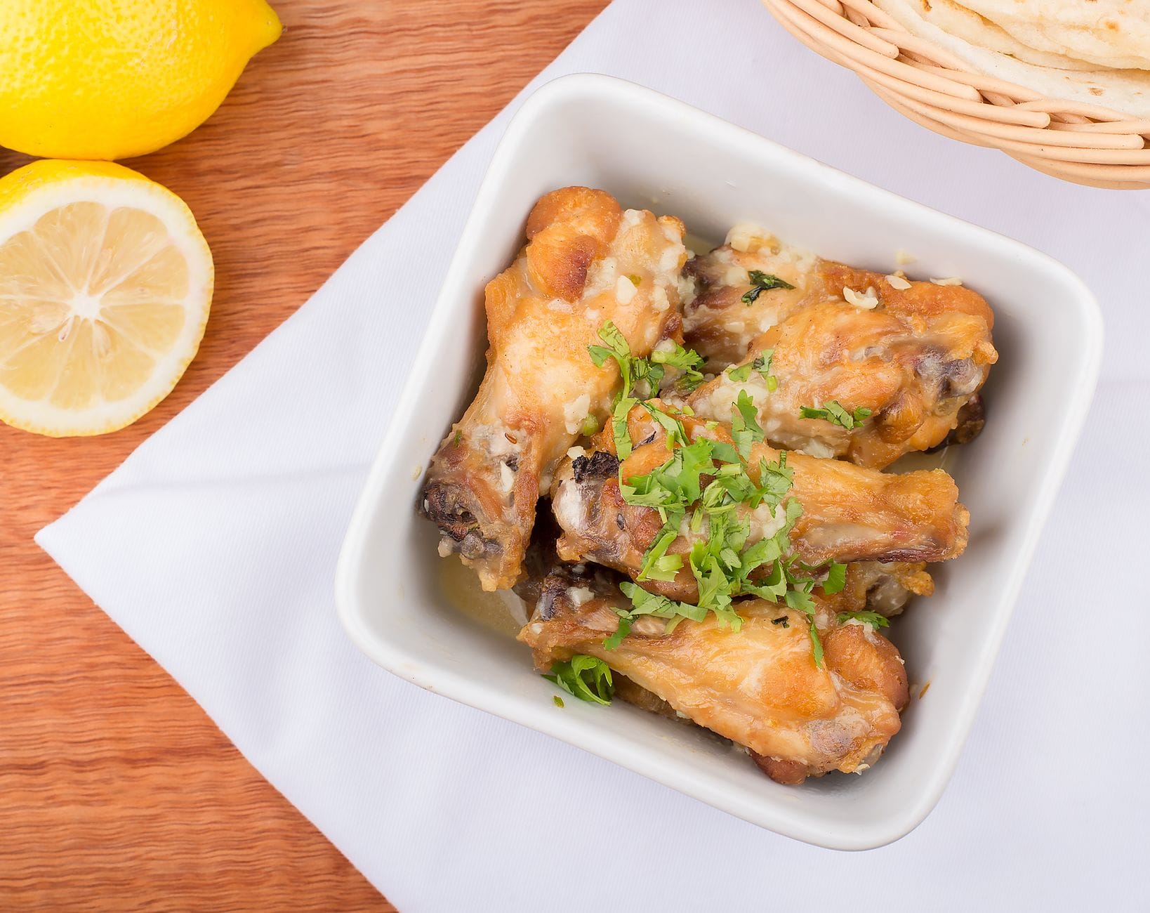 Baked chicken pieces in a white dish topped with fresh coriander, lemon alongside
