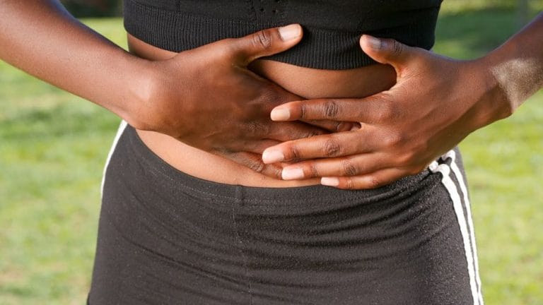 Close-up of a person outdoors in black sportswear pressing both hands against their abdomen