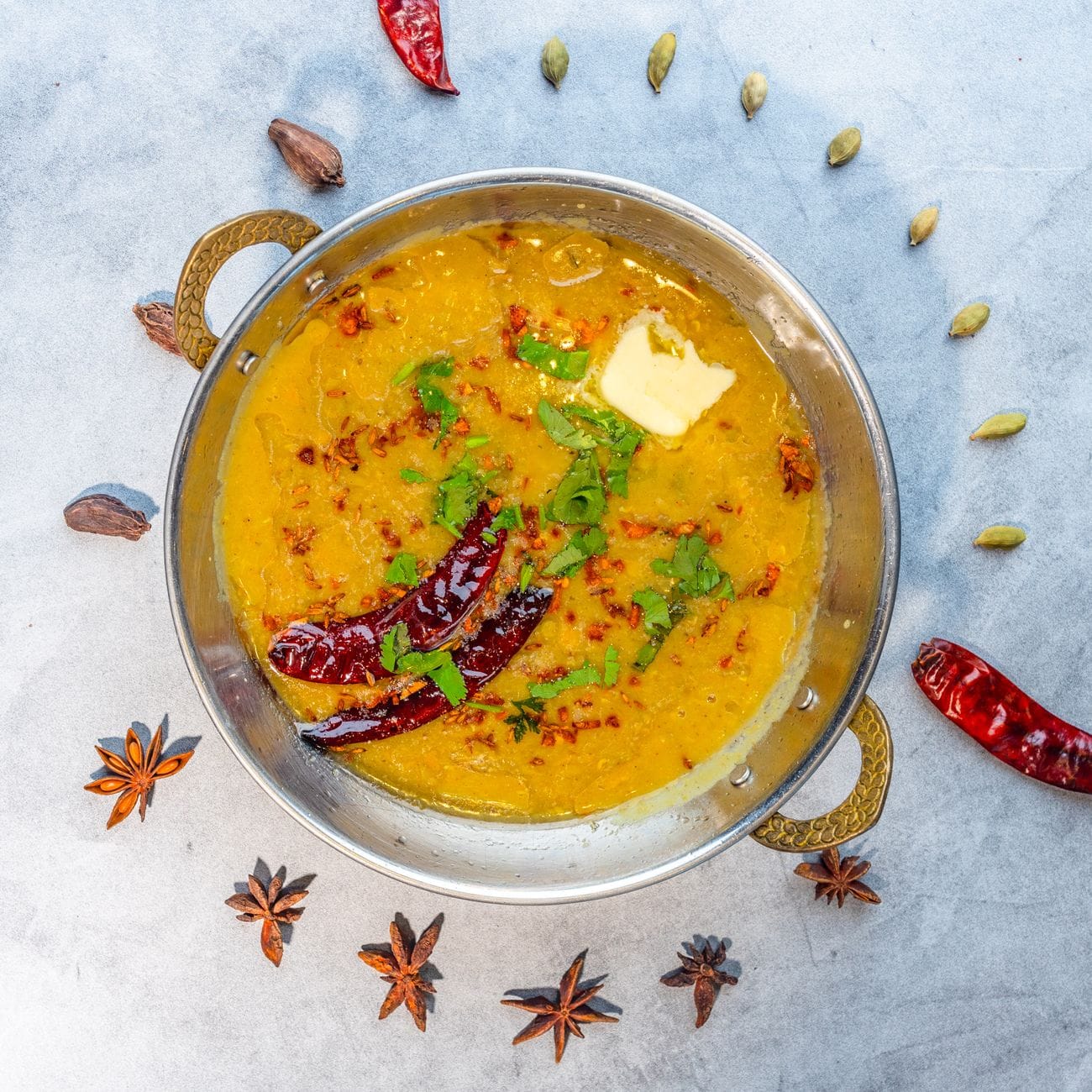 Yellow dal tadka topped with dried red chilies, cilantro and butter in a brass-handled bowl