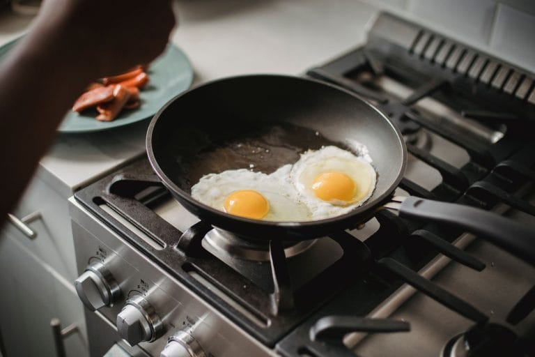 Two fried eggs cooking in a dark non-stick frying pan on a gas hob