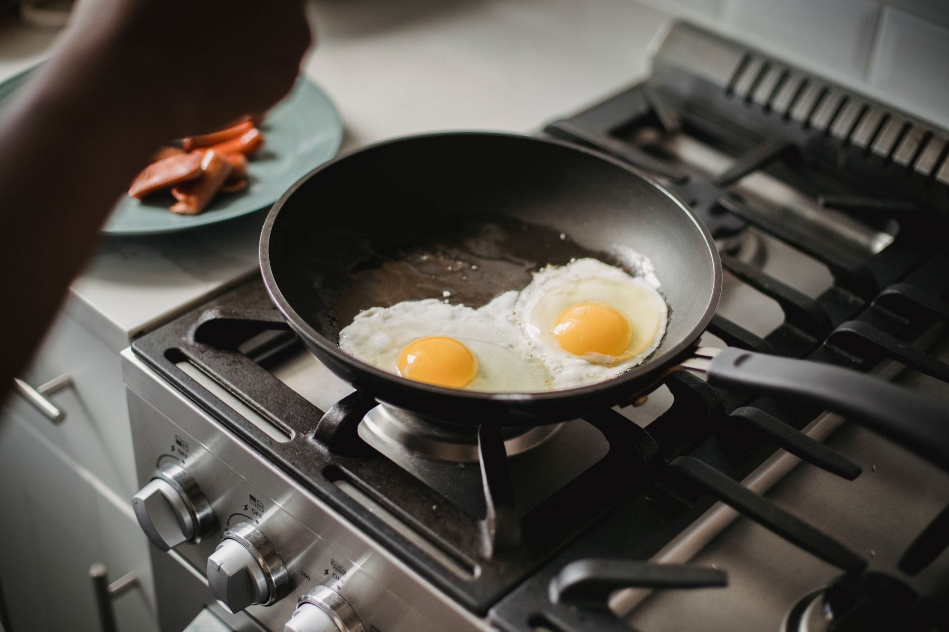 Two fried eggs cooking in a dark non-stick frying pan on a gas hob