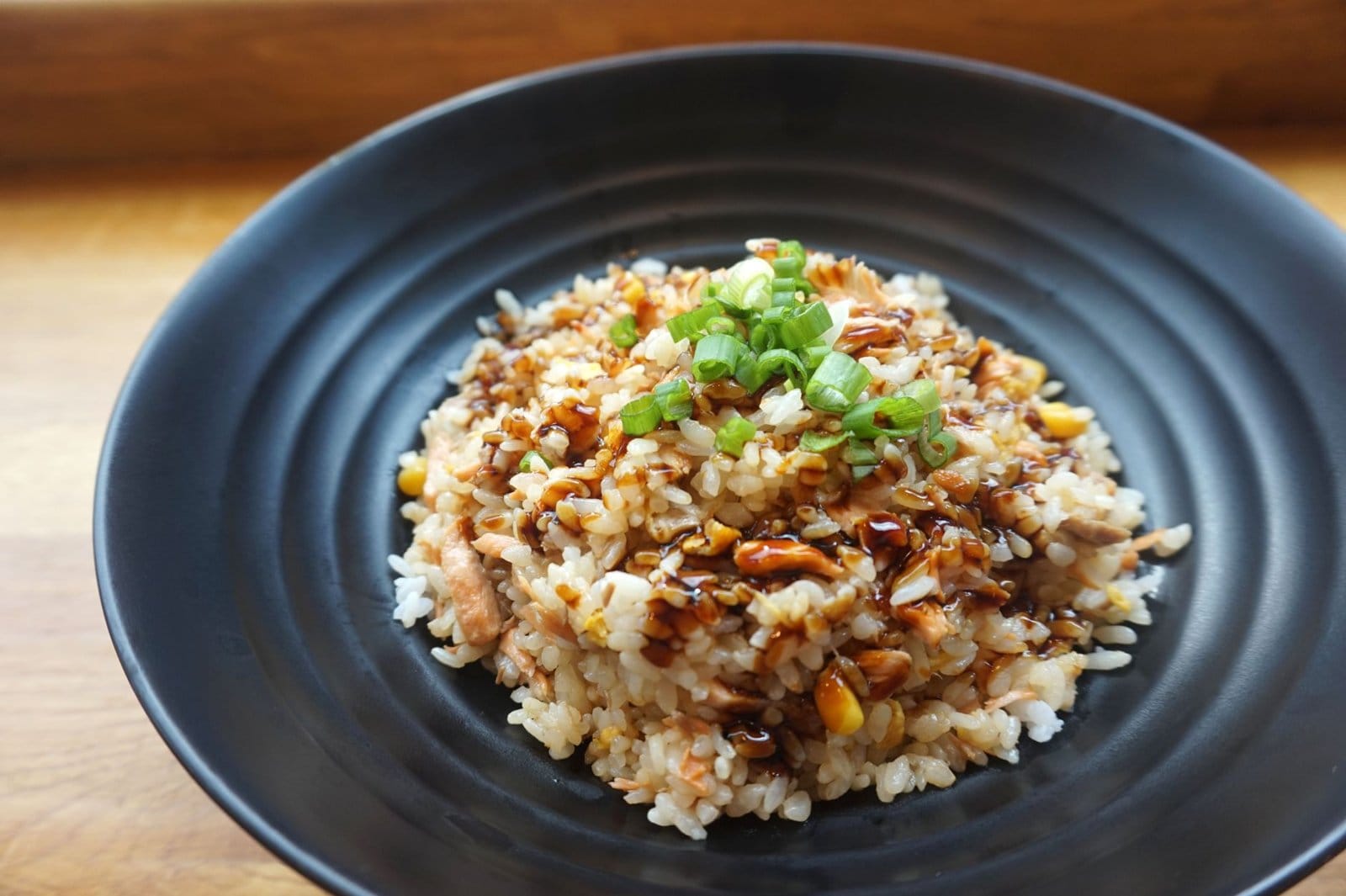 Plate of fried rice topped with sliced spring onion and a drizzle of dark sauce