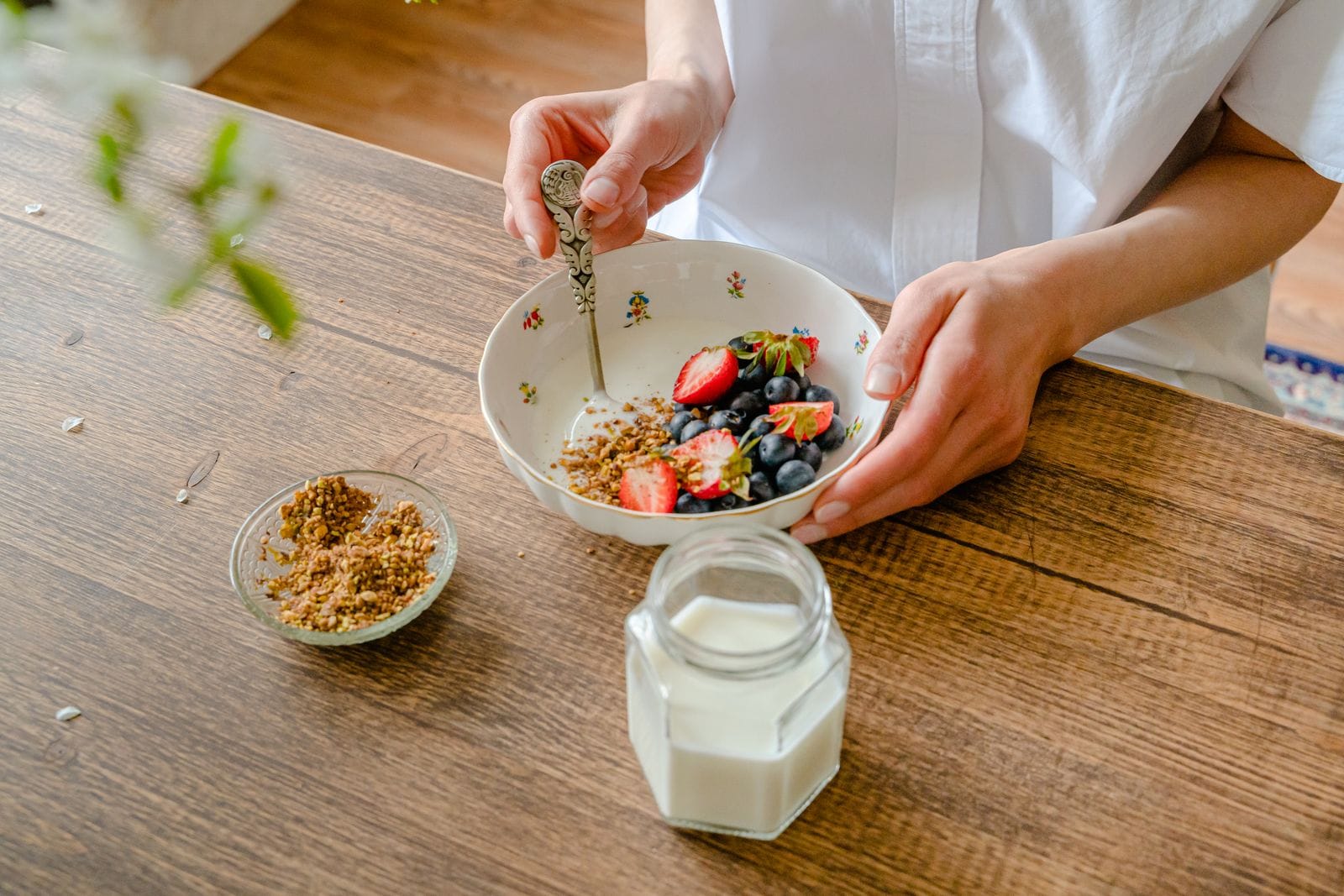 Bowl of yogurt topped with strawberries, blueberries and granola held over a wooden table