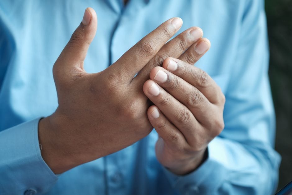 Close-up of a person in a blue shirt holding and pressing the fingers of one hand with the other