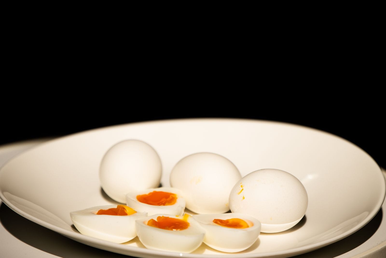 Whole and halved hard-boiled eggs on a white plate against a dark background