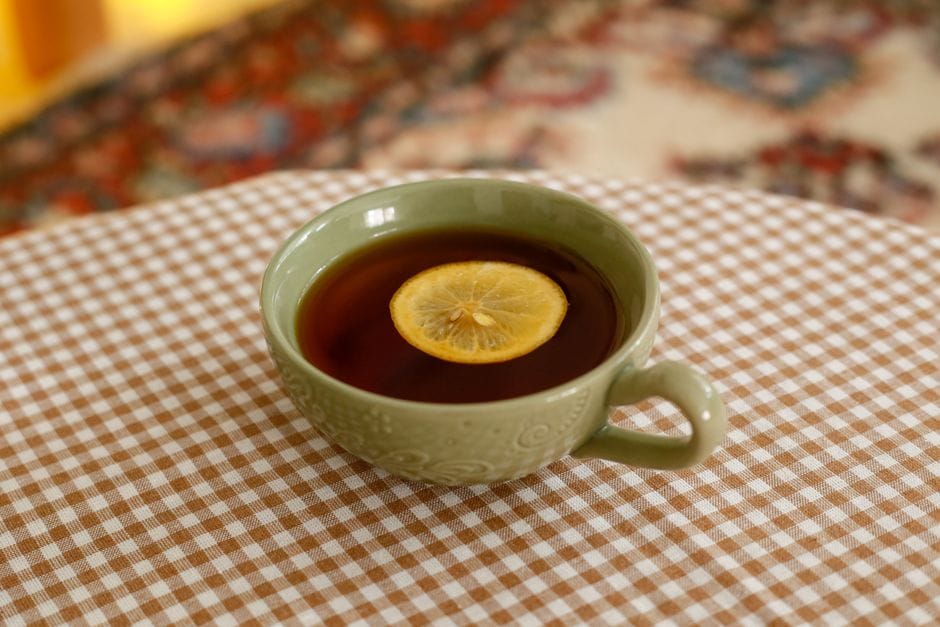Cup of hot tea with a lemon slice in a green ceramic cup on a checked tablecloth