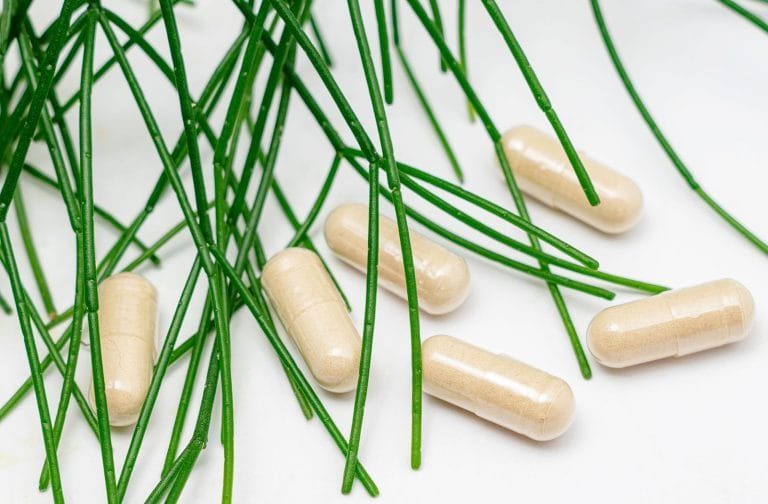 Beige supplement capsules scattered among thin green stems on a white surface