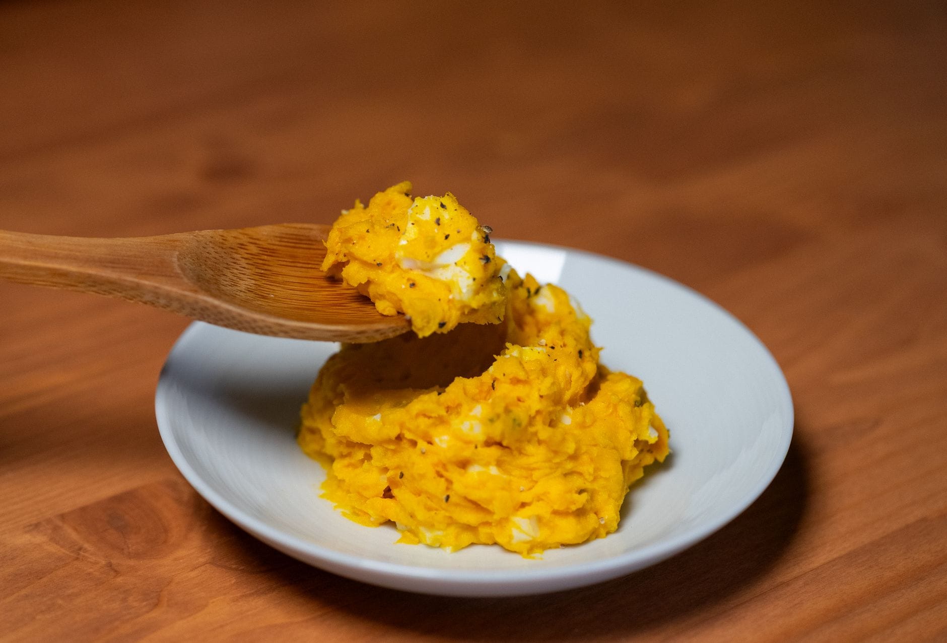 Wooden spoon holding a mound of thick mashed pumpkin that keeps its shape