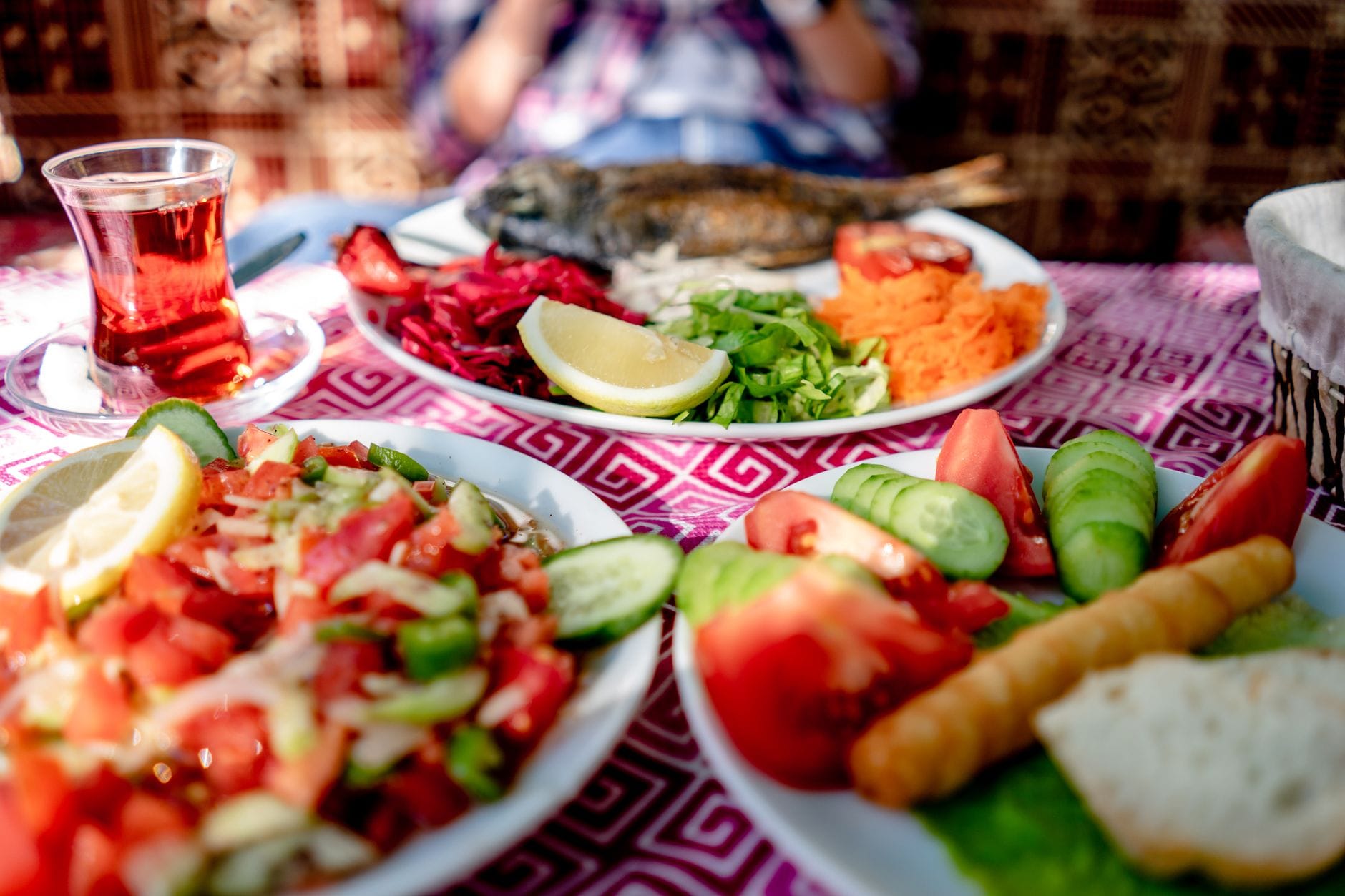 Mediterranean table with grilled whole fish, chopped tomato and cucumber salads, bread and a glass of tea