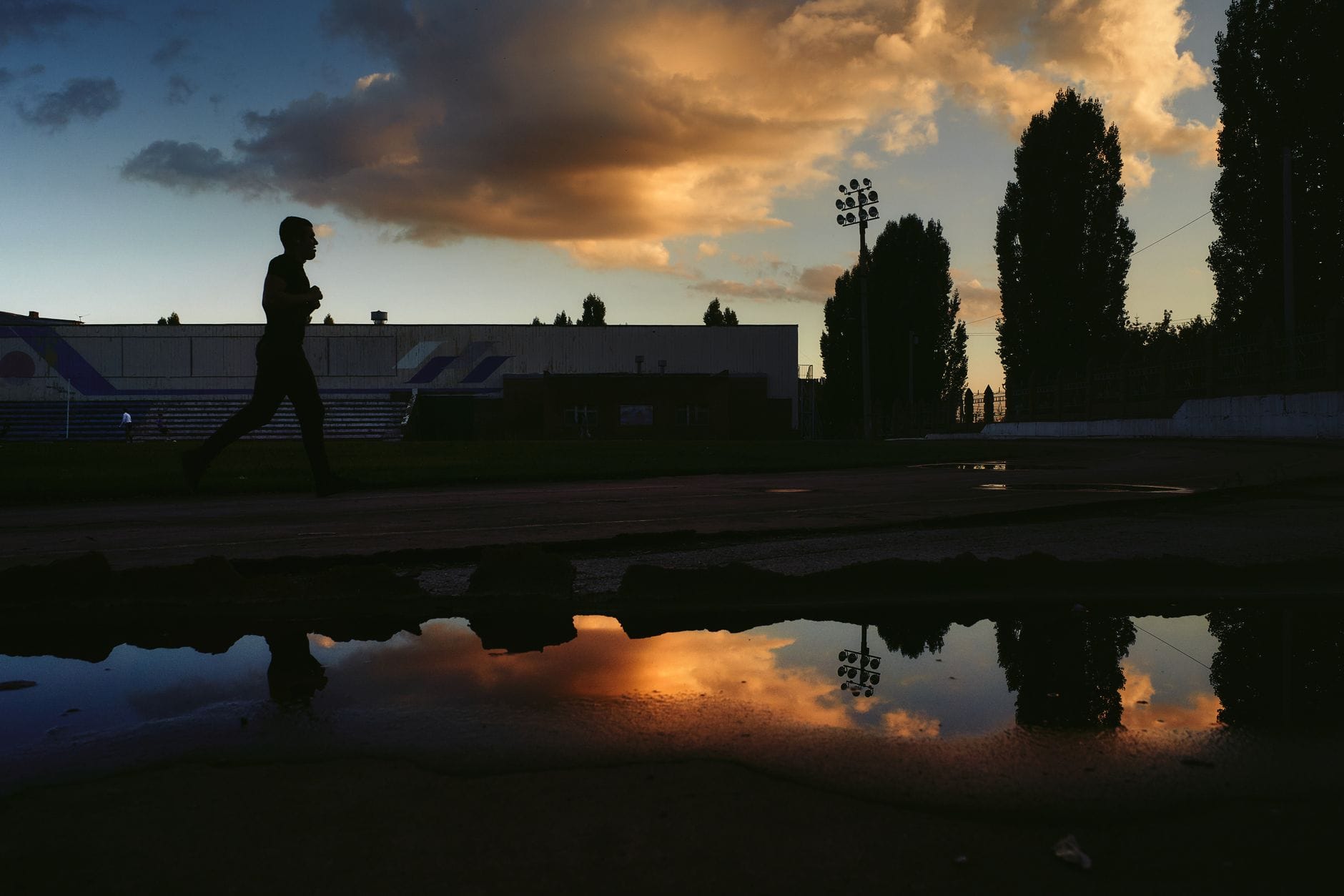 Runner silhouetted against a sunset sky, reflected in a puddle beside a track