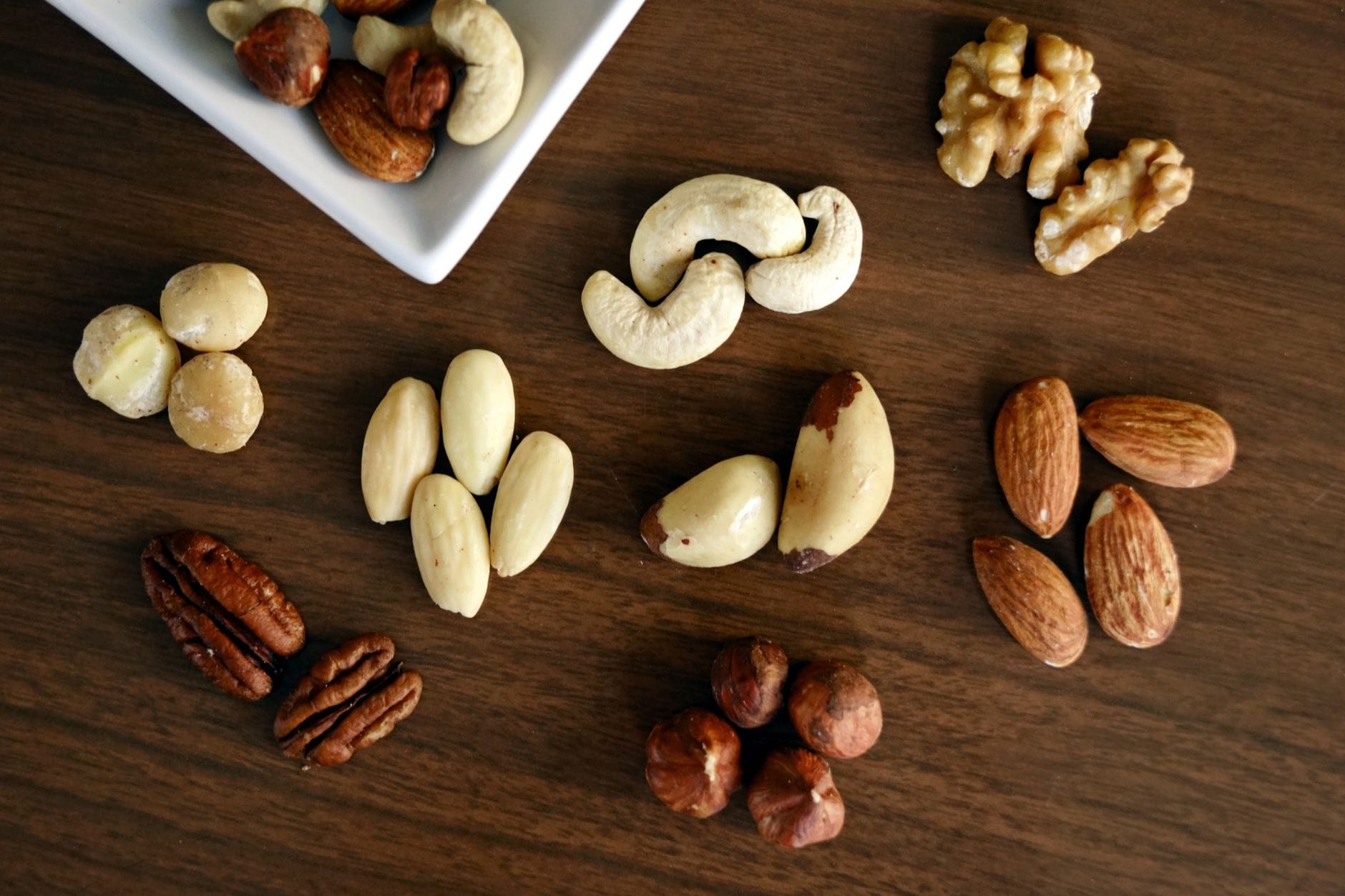 Pecans, hazelnuts, walnuts, almonds and cashews arranged in groups on dark wood