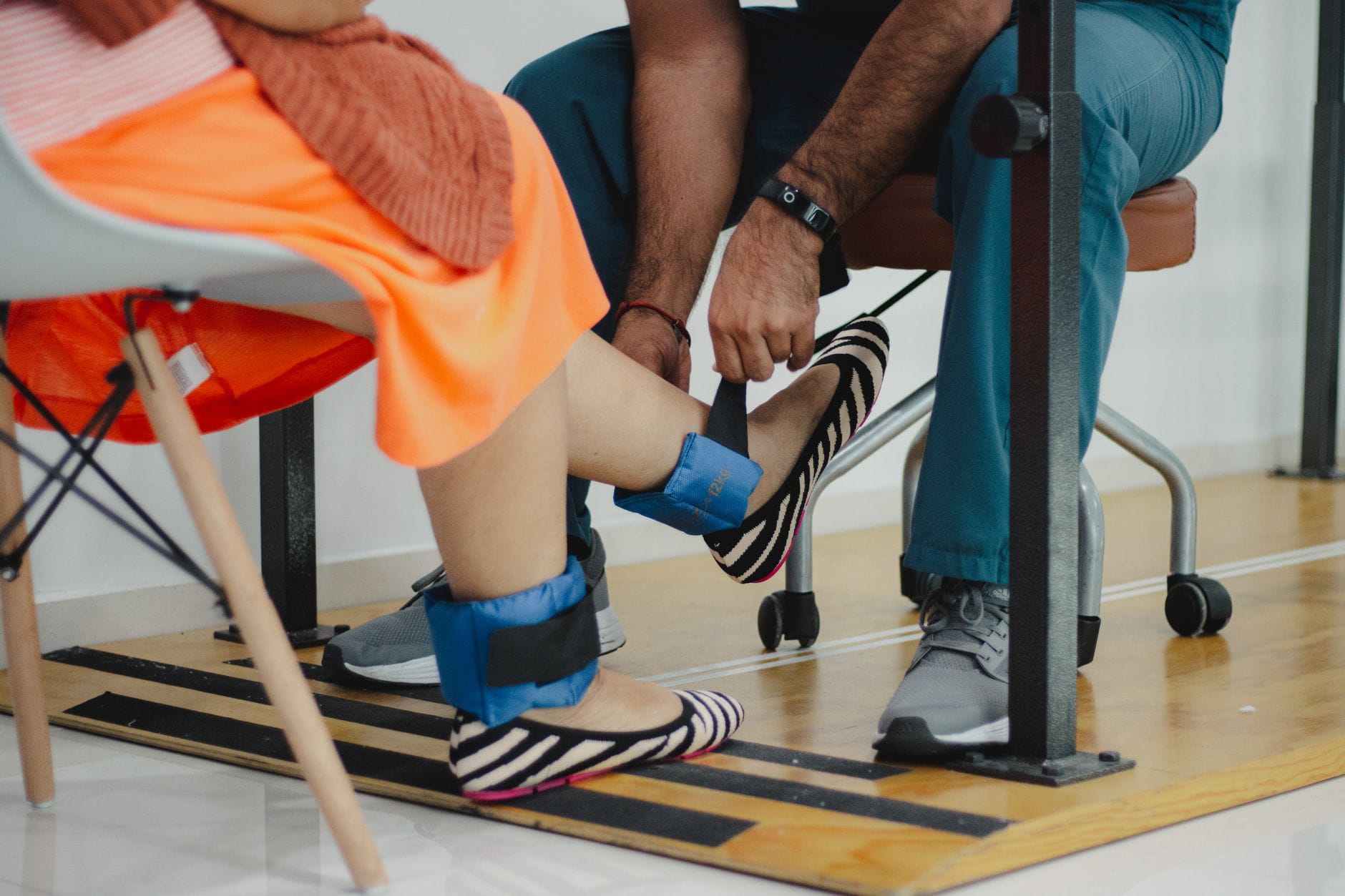 Therapist fastening blue velcro ankle weights around a seated patient's ankles
