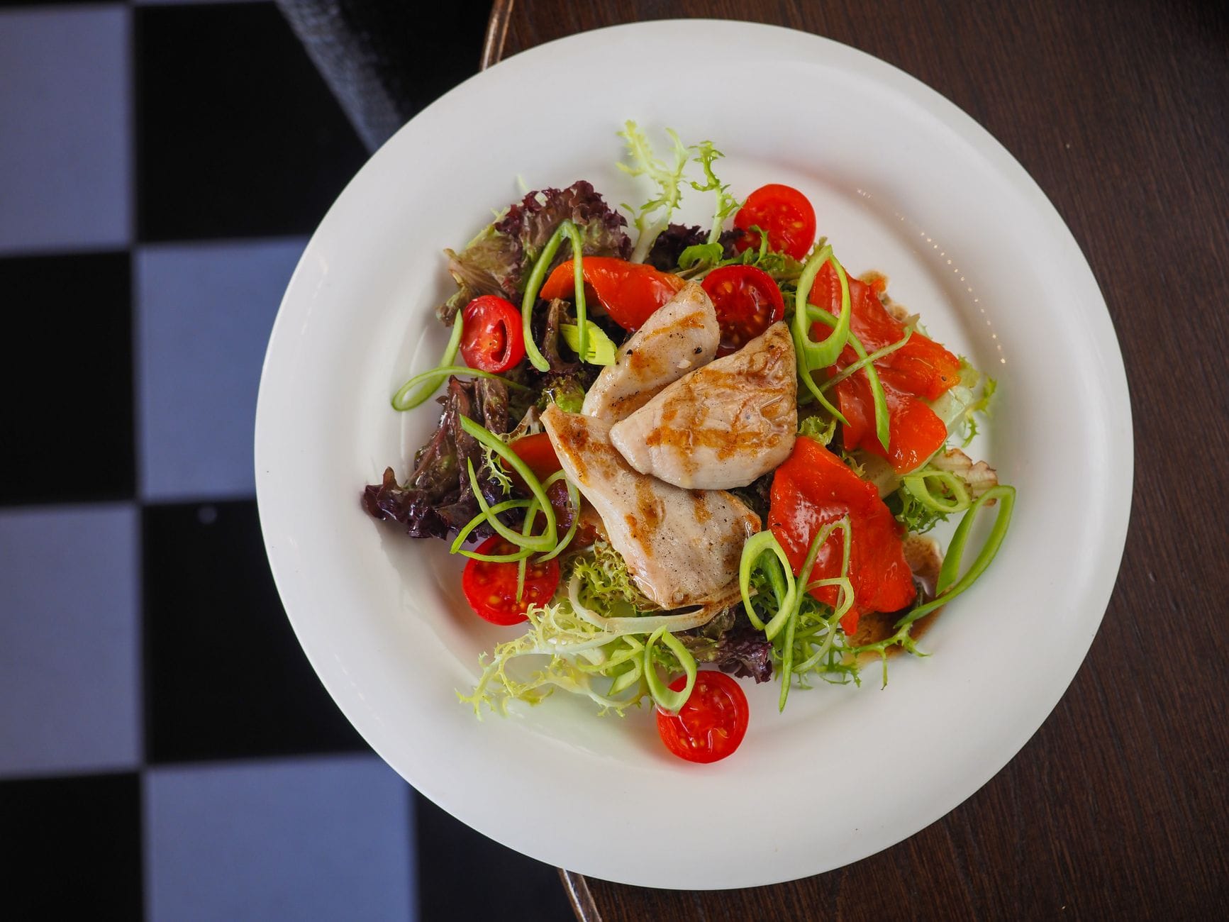 Plate of sliced grilled chicken with salad leaves, cherry tomatoes and spring onion