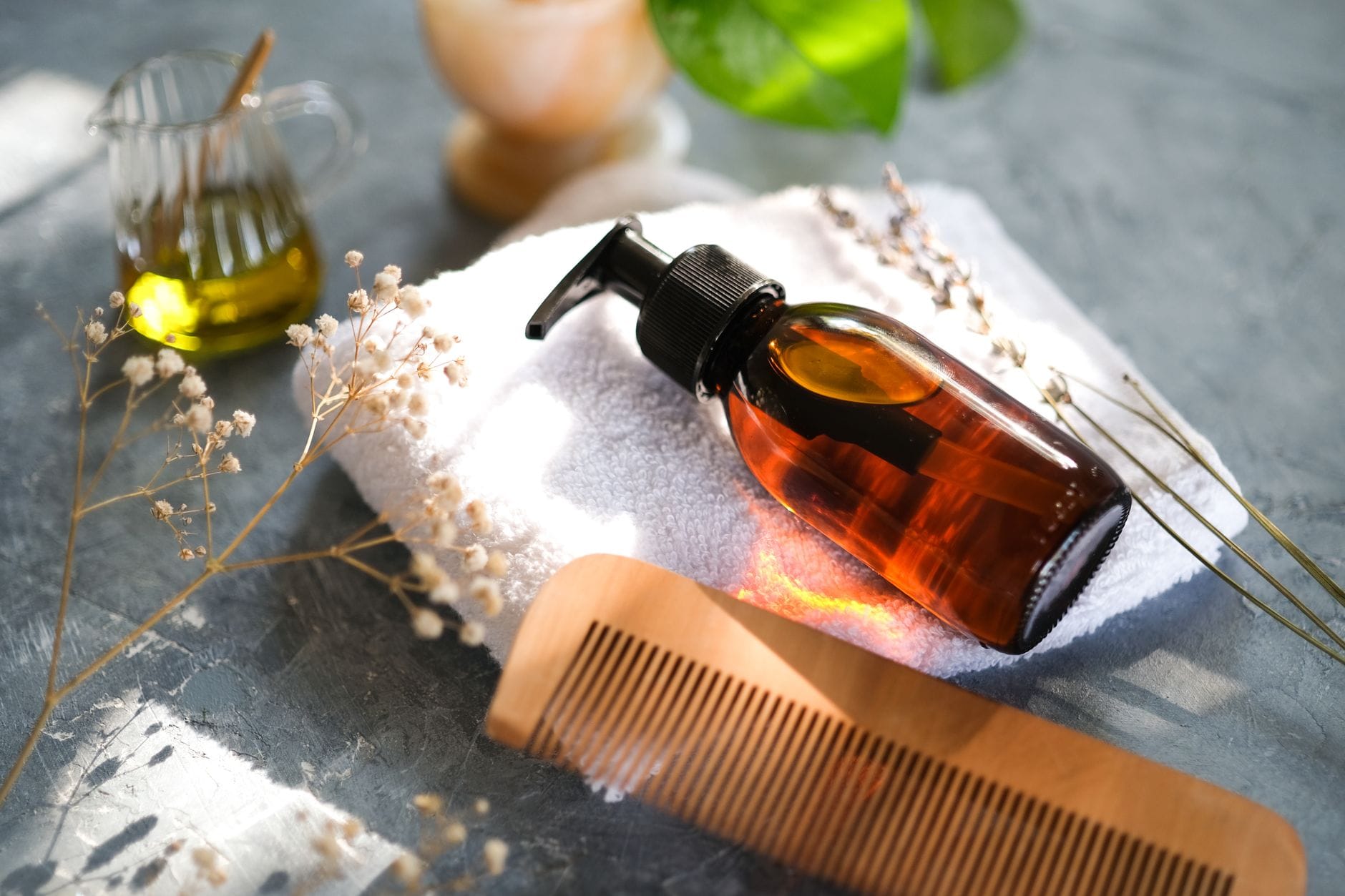 Amber pump bottle of hair oil on a towel beside a wooden comb
