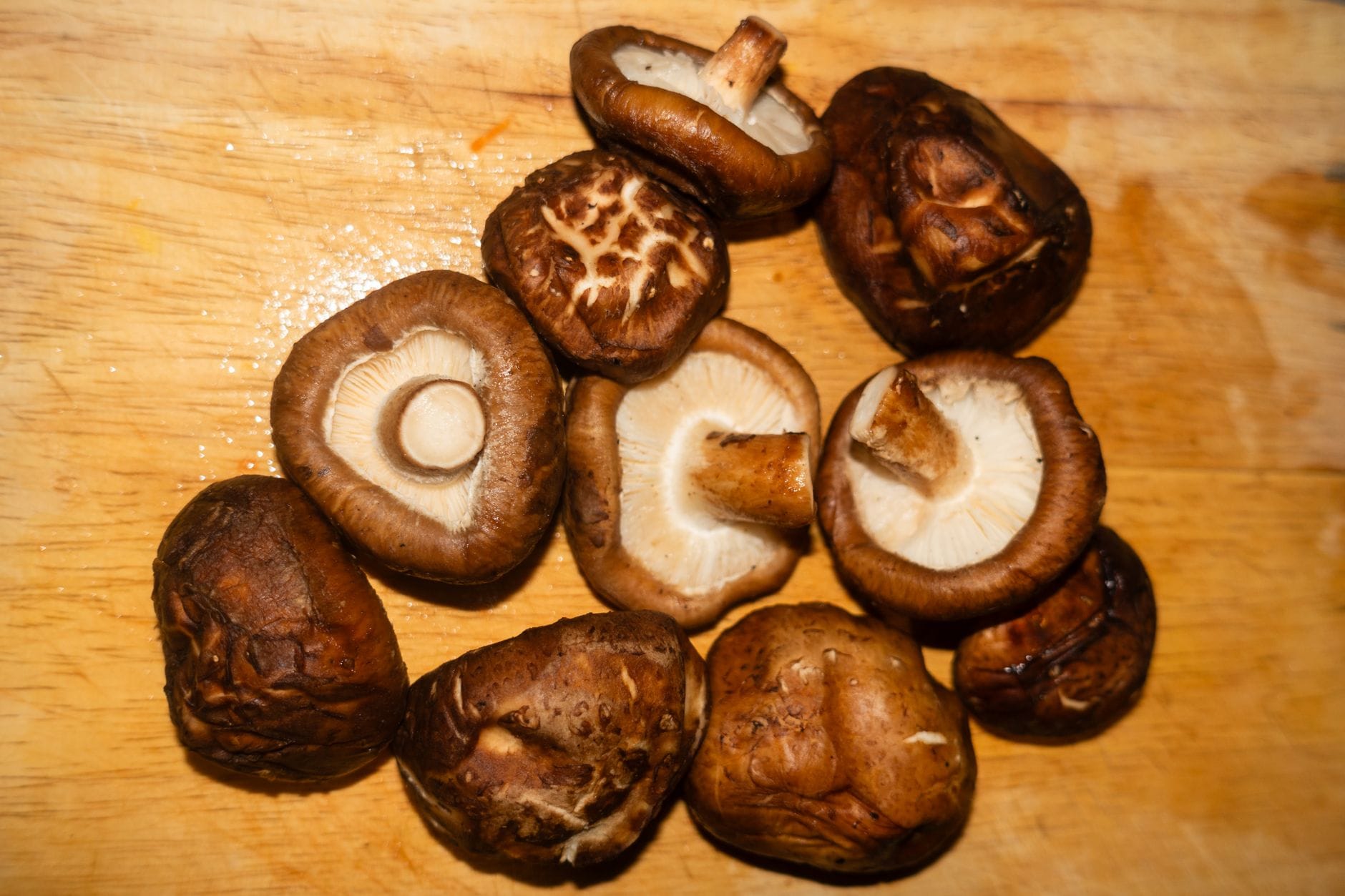 Fresh shiitake mushrooms with dark domed caps and cream gills on a wooden board