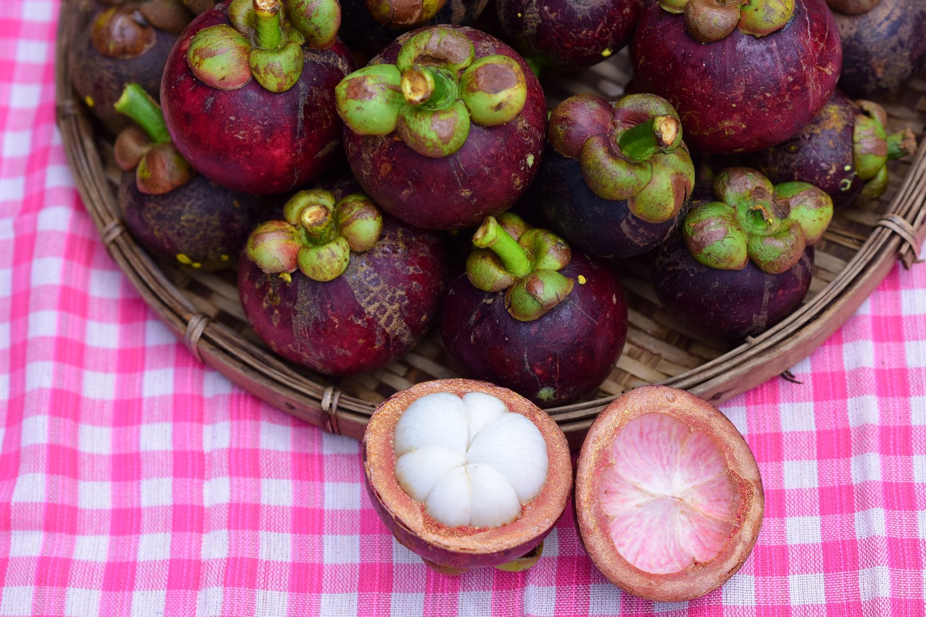 Purple mangosteens in a basket with one cut open showing white flesh