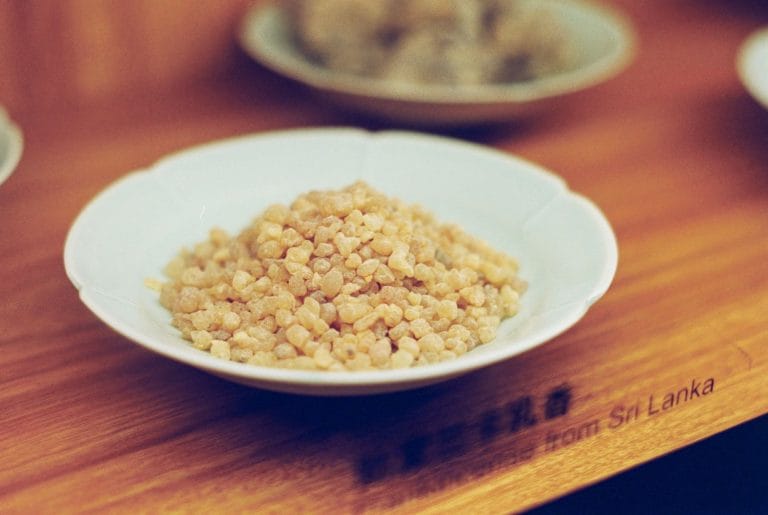 Pale frankincense resin granules heaped in a small white dish on a wooden counter
