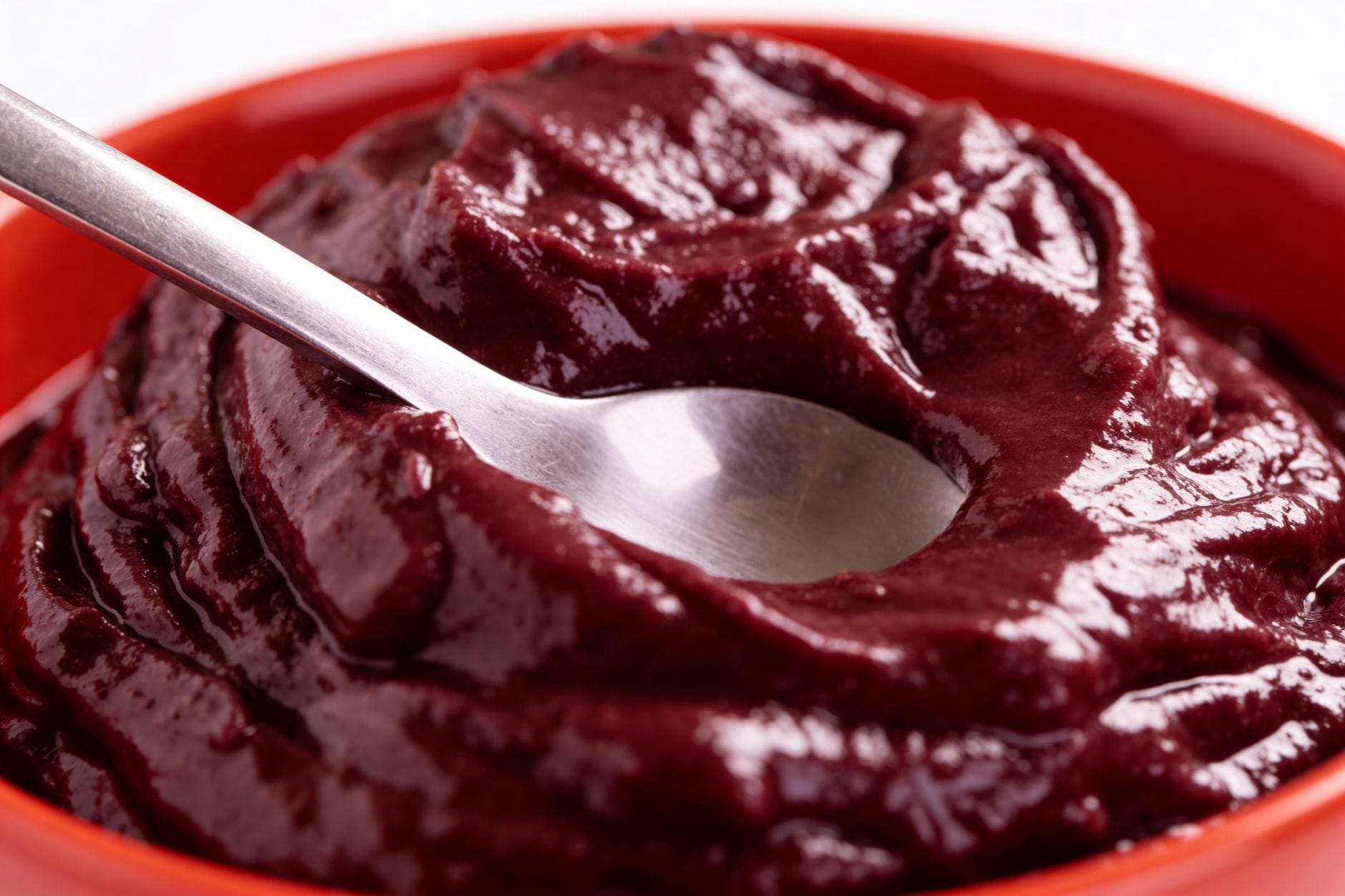 Spoon resting in a bowl of thick, completely smooth deep-red puree