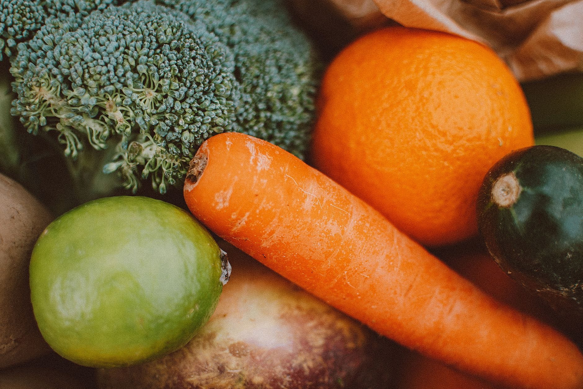 Close-up of broccoli, a carrot, a lime, an orange and an avocado in a paper bag