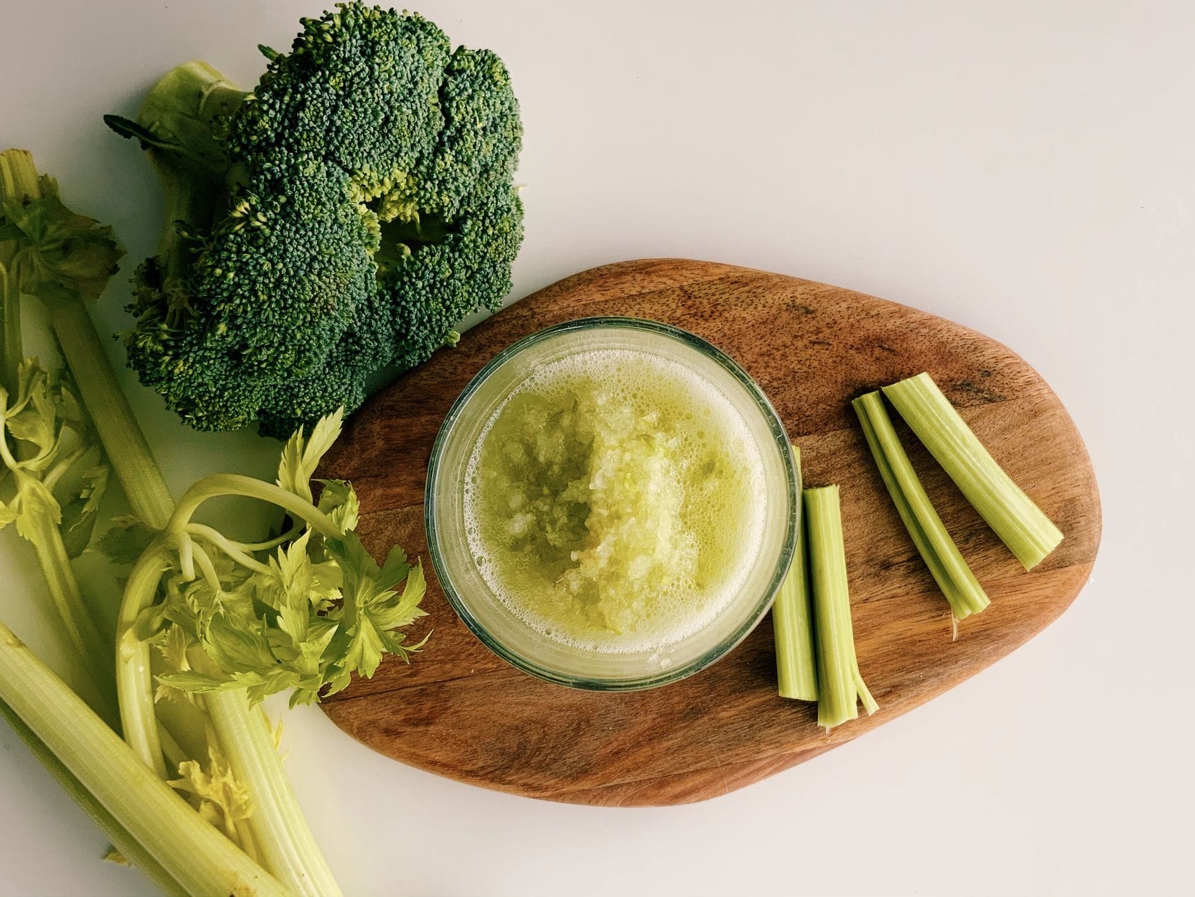 Glass of pale green celery juice beside fresh celery stalks on a board