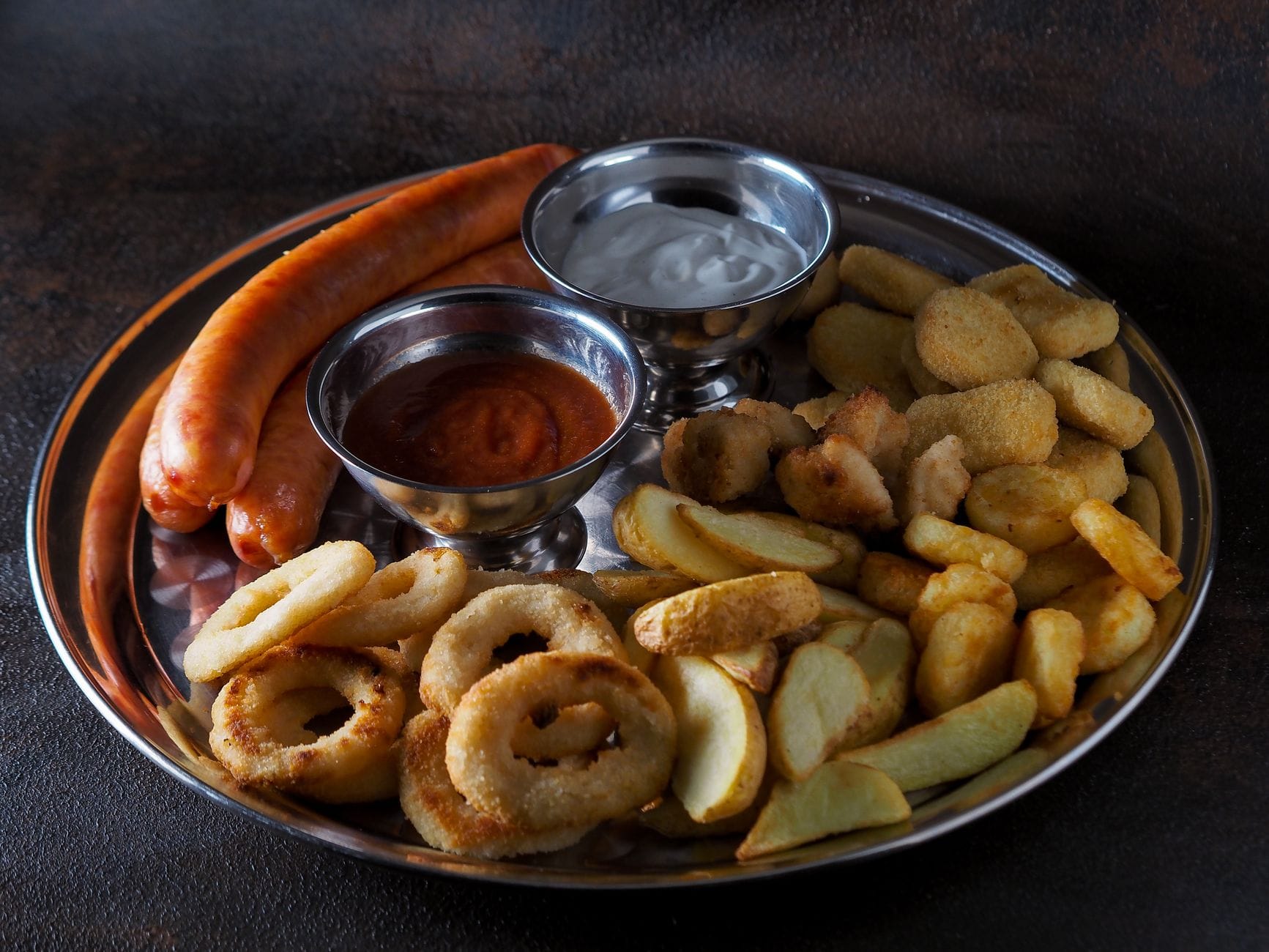 Metal platter of sausages, breaded nuggets, onion rings, fries and dips