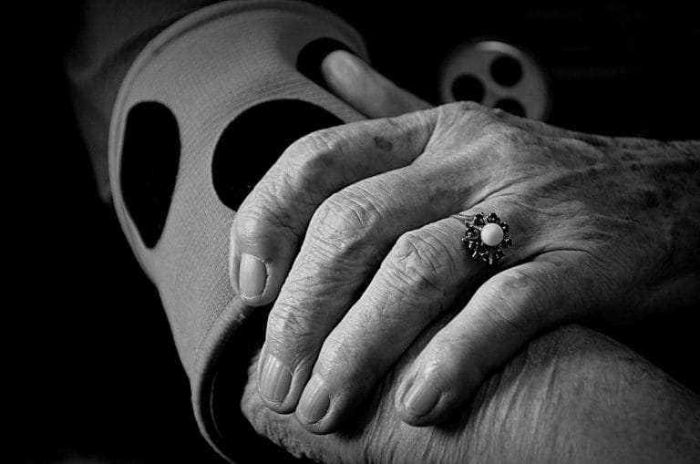 Black and white close-up of an older person's clasped hands resting in their lap