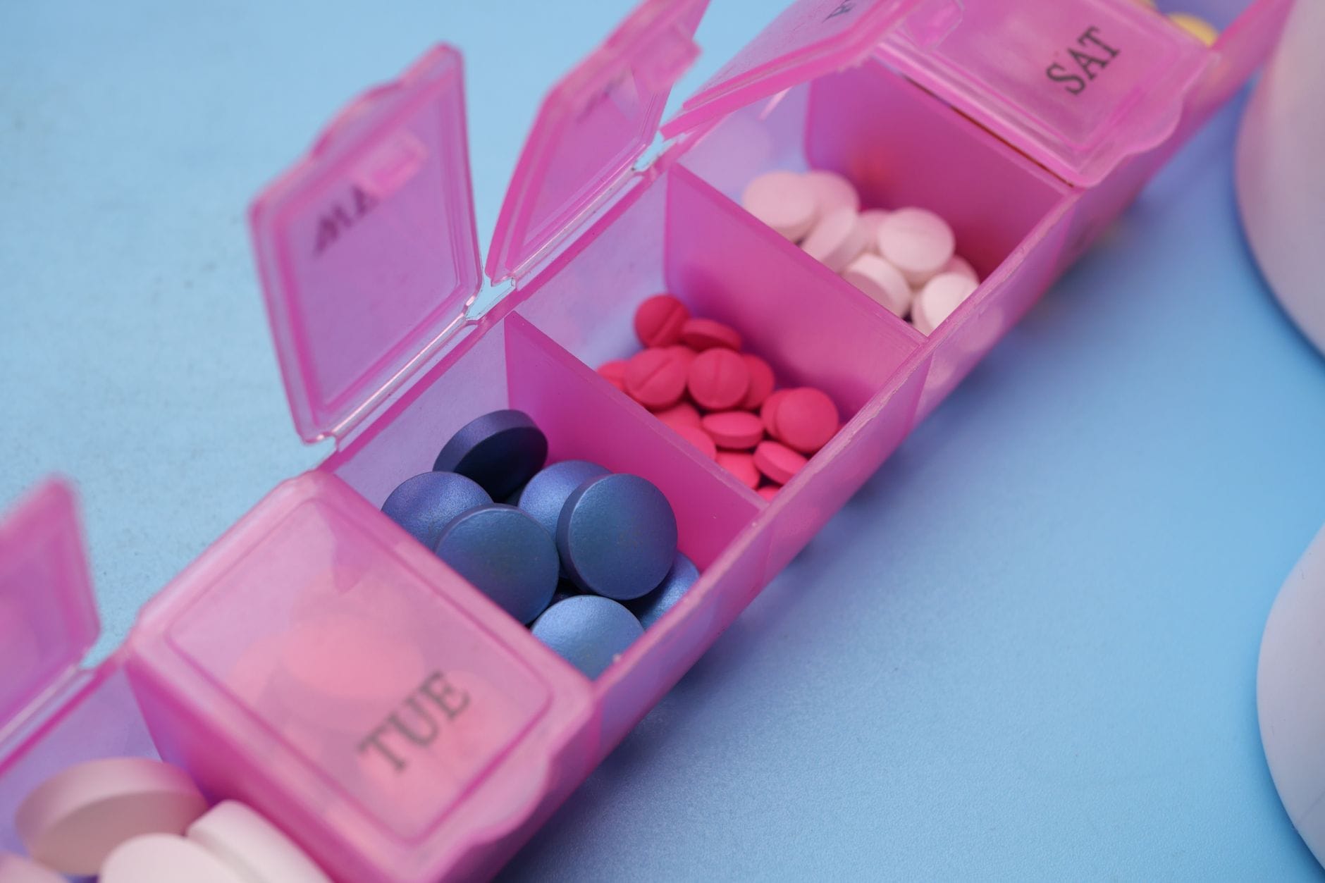 Open pink weekly pill organizer with different coloured tablets in the daily compartments