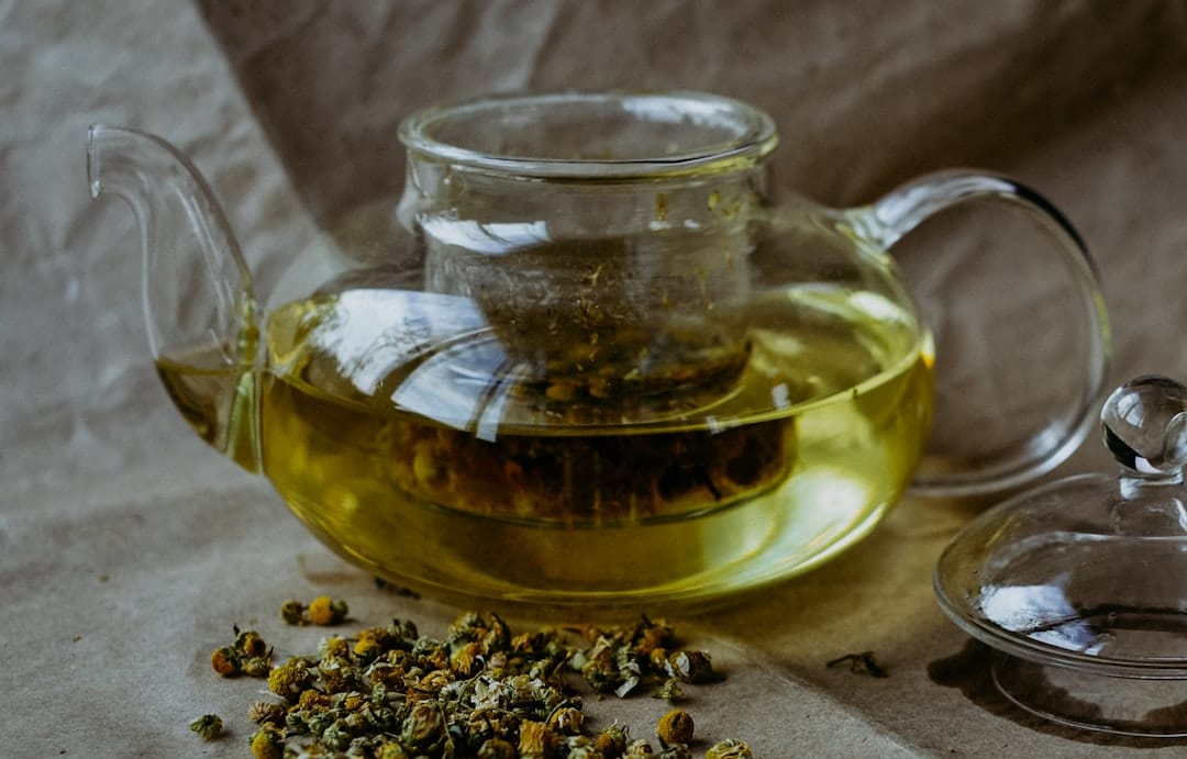Glass teapot of pale herbal infusion with dried flowers scattered beside it