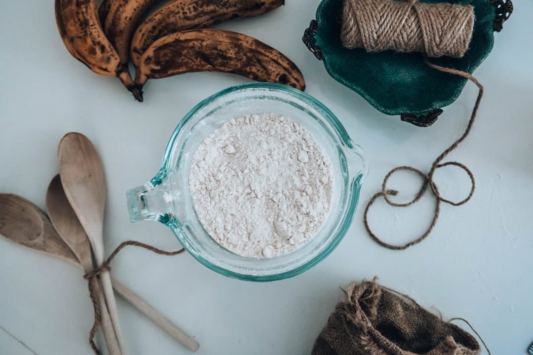 Glass jug of fine white flour beside wooden spoons and overripe bananas
