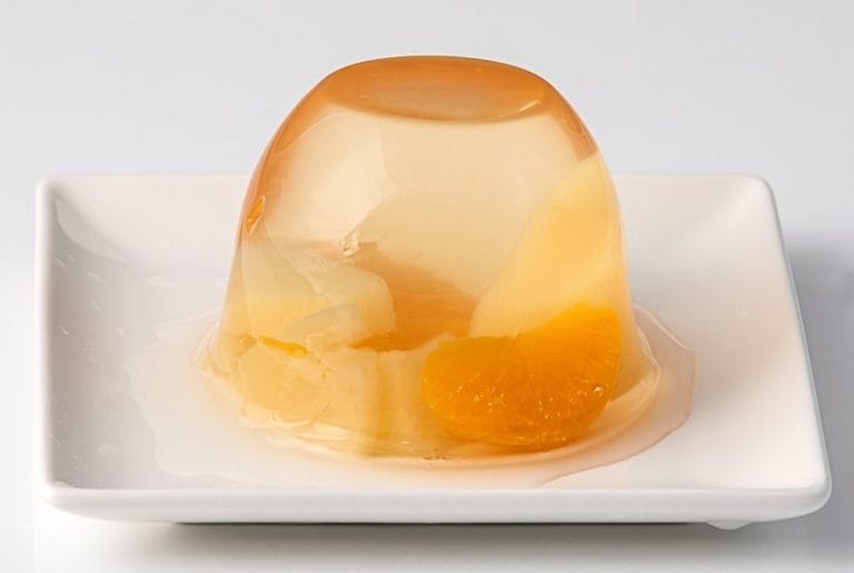 A single dome of clear amber jelly set with pieces of mandarin and pear on a white plate
