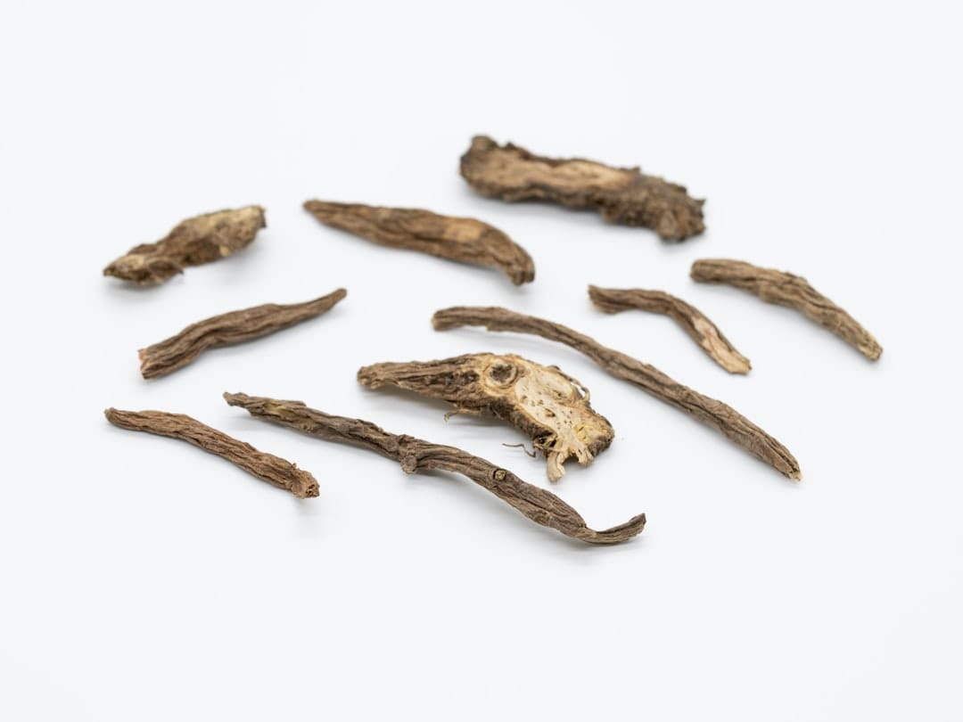 Dried medicinal root pieces with fibrous bark and pale yellow interior on white