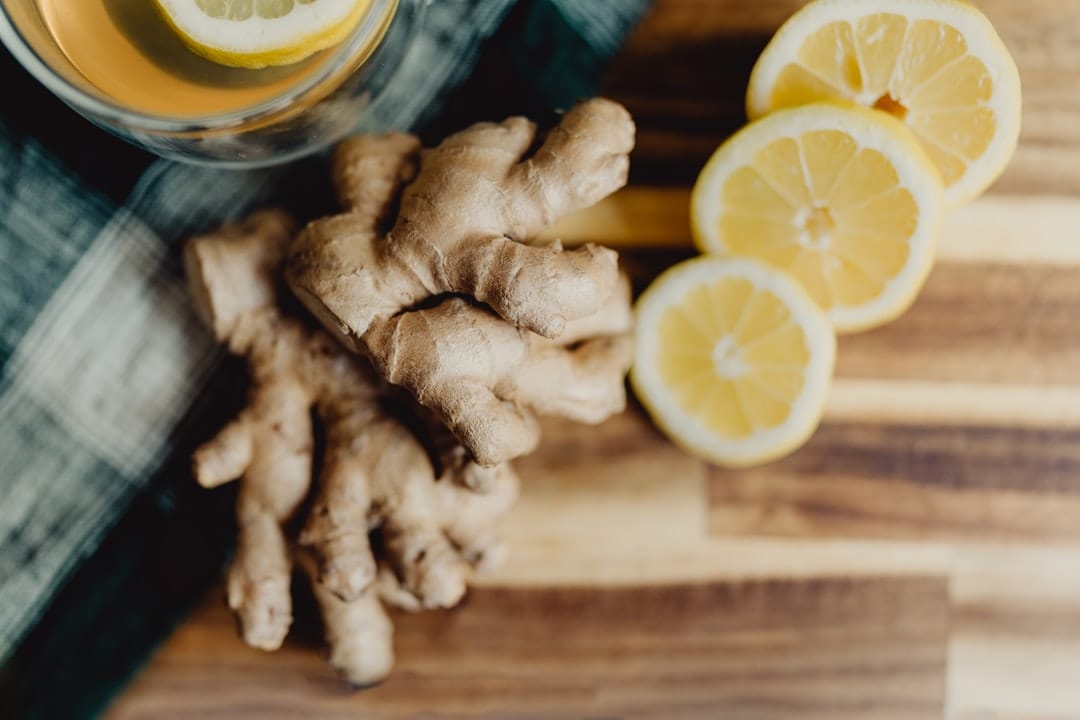 Fresh ginger root and lemon slices beside a glass of tea on a wooden board
